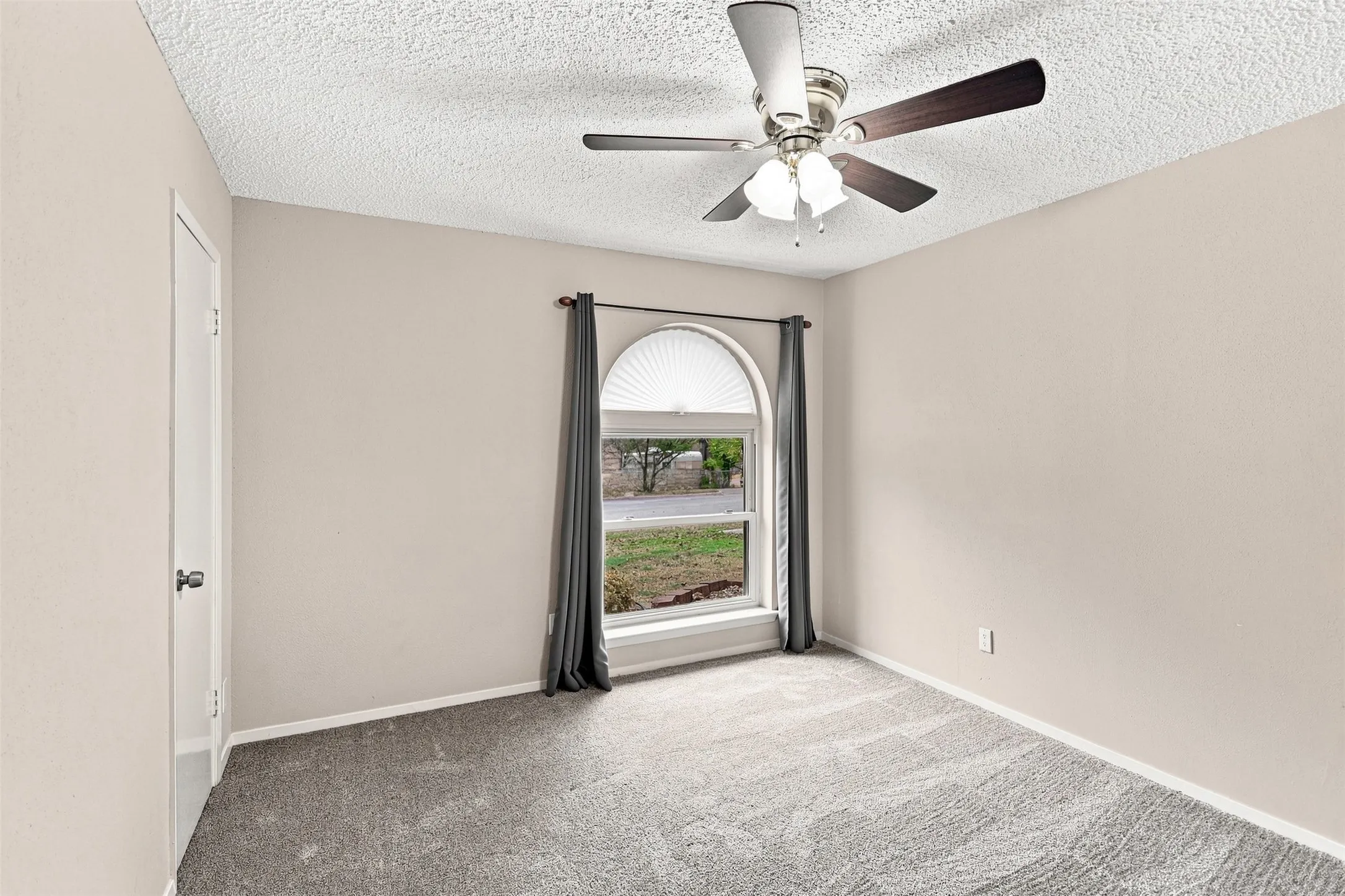 Arched window with light-filtering blinds, textured ceiling, ceiling fan with light fixture, and neutral-toned walls