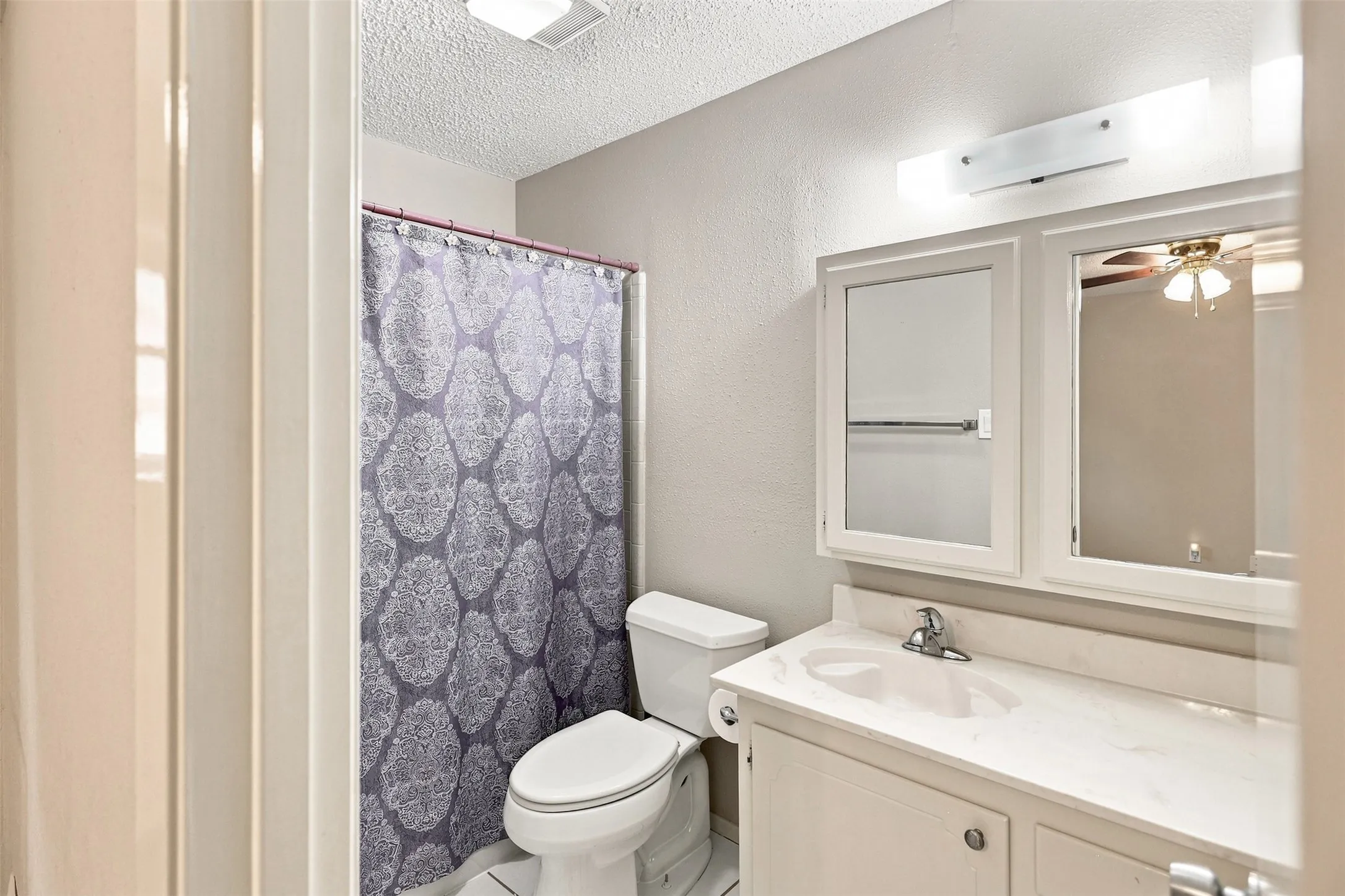 Bathroom featuring a white vanity with integrated sink, dual mirrored medicine cabinets, wall-mounted light fixture, and a toilet