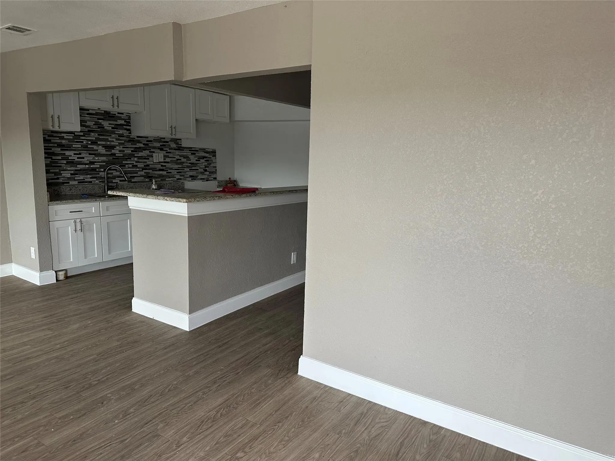 Open-concept kitchen featuring white cabinetry, a granite-style countertop, and a mosaic tile backsplash