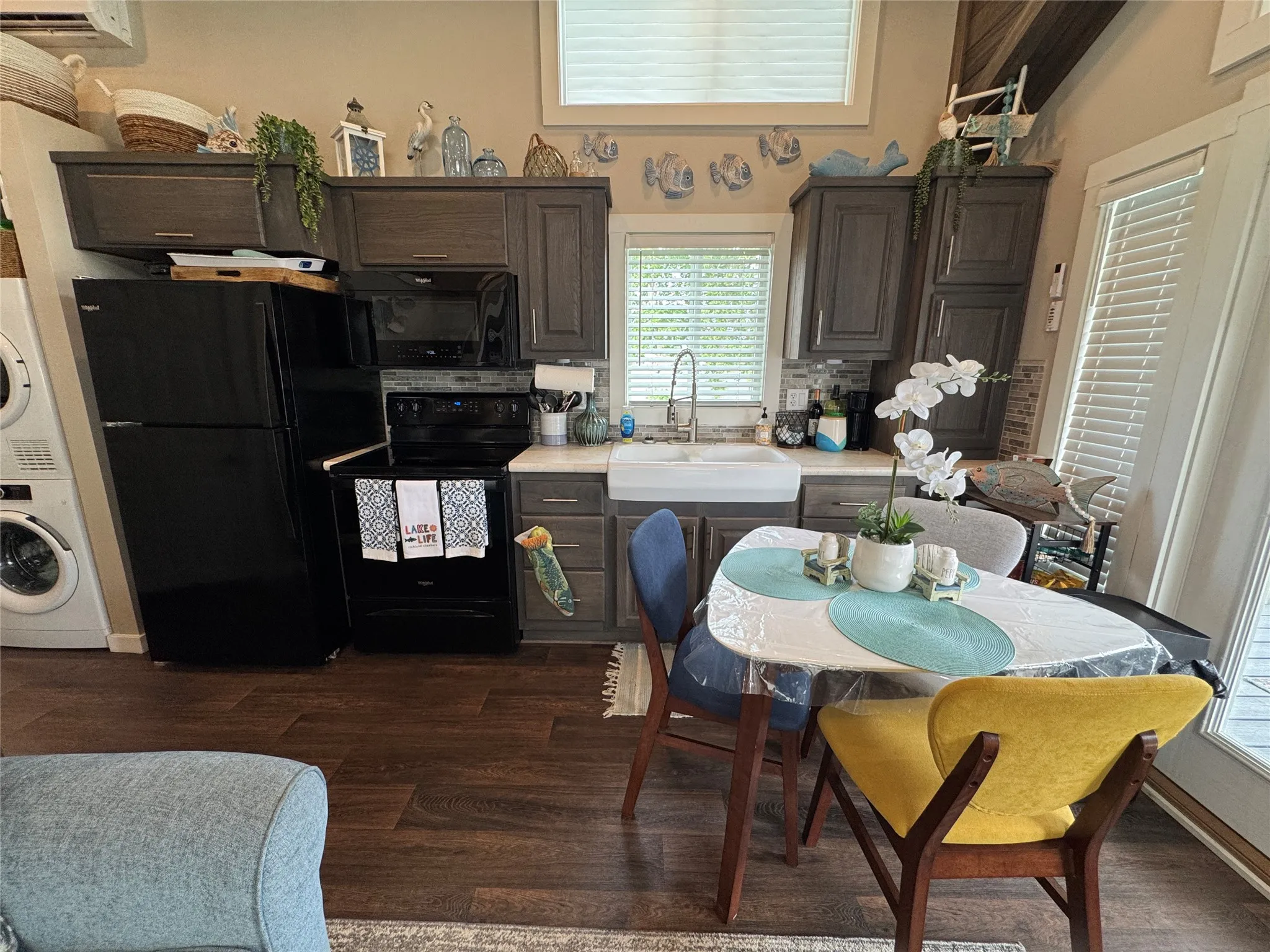 Kitchen area featuring wood-finish flooring, dark wood cabinetry, white farmhouse sink, and a gray subway tile backsplash