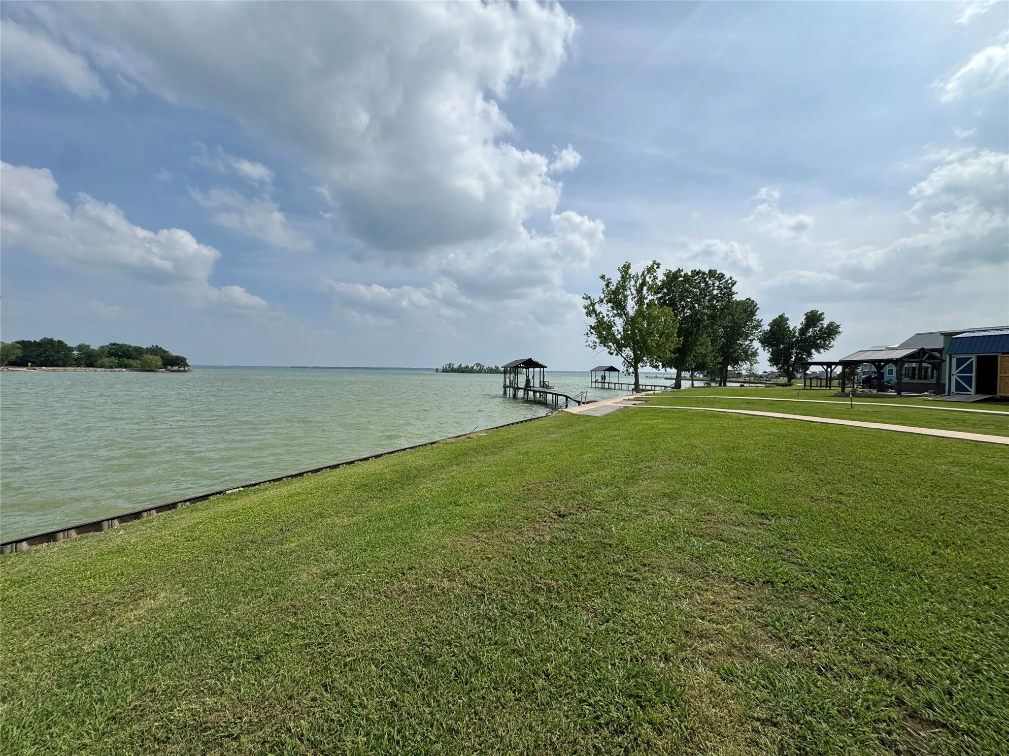 Expansive waterfront property featuring a large grassy lawn, private dock with covered boat slip, additional covered dock, mature trees, and a visible portion of a residential structure