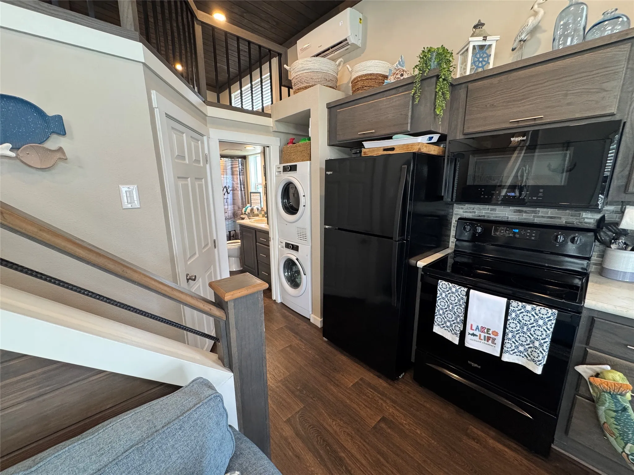 Compact kitchen featuring black appliances, wood-finish flooring, a tile backsplash, and dark wood-look cabinetry