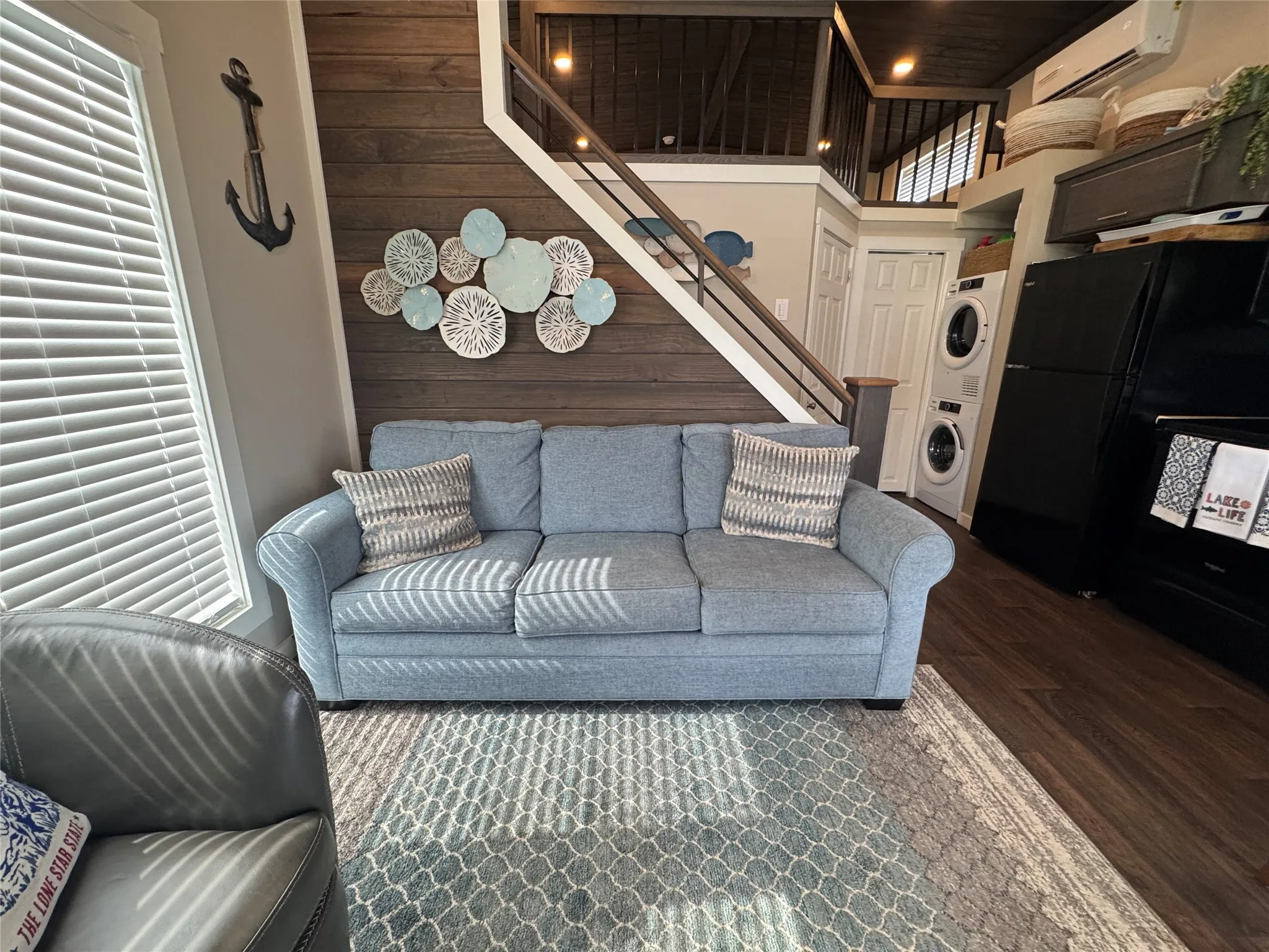 Open-concept living area with wood-finish flooring, a contemporary staircase featuring metal spindles, and an integrated laundry area with a stacked washer and dryer