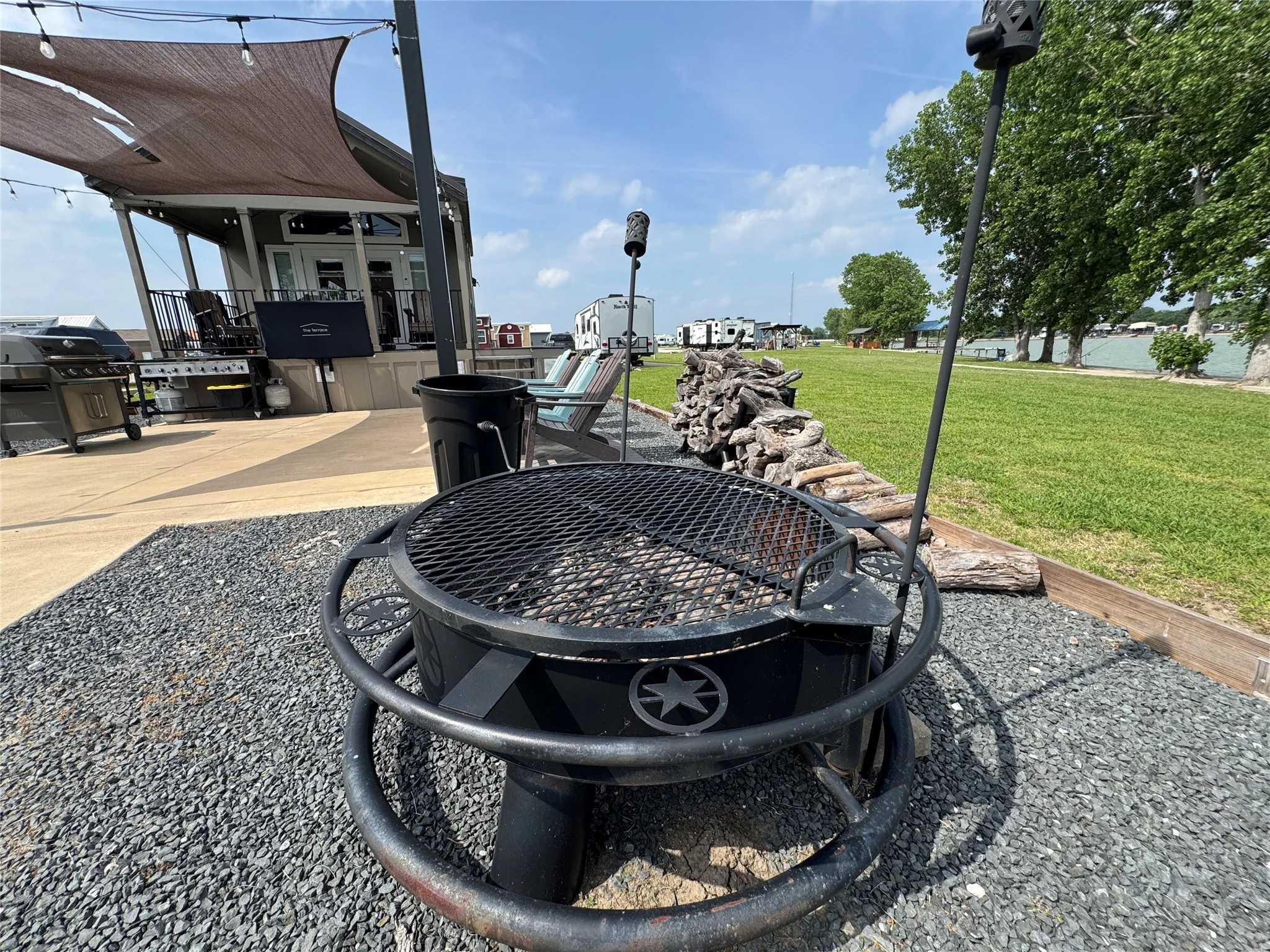 Outdoor fire pit area featuring a gravel base, adjacent concrete patio, and a water backdrop