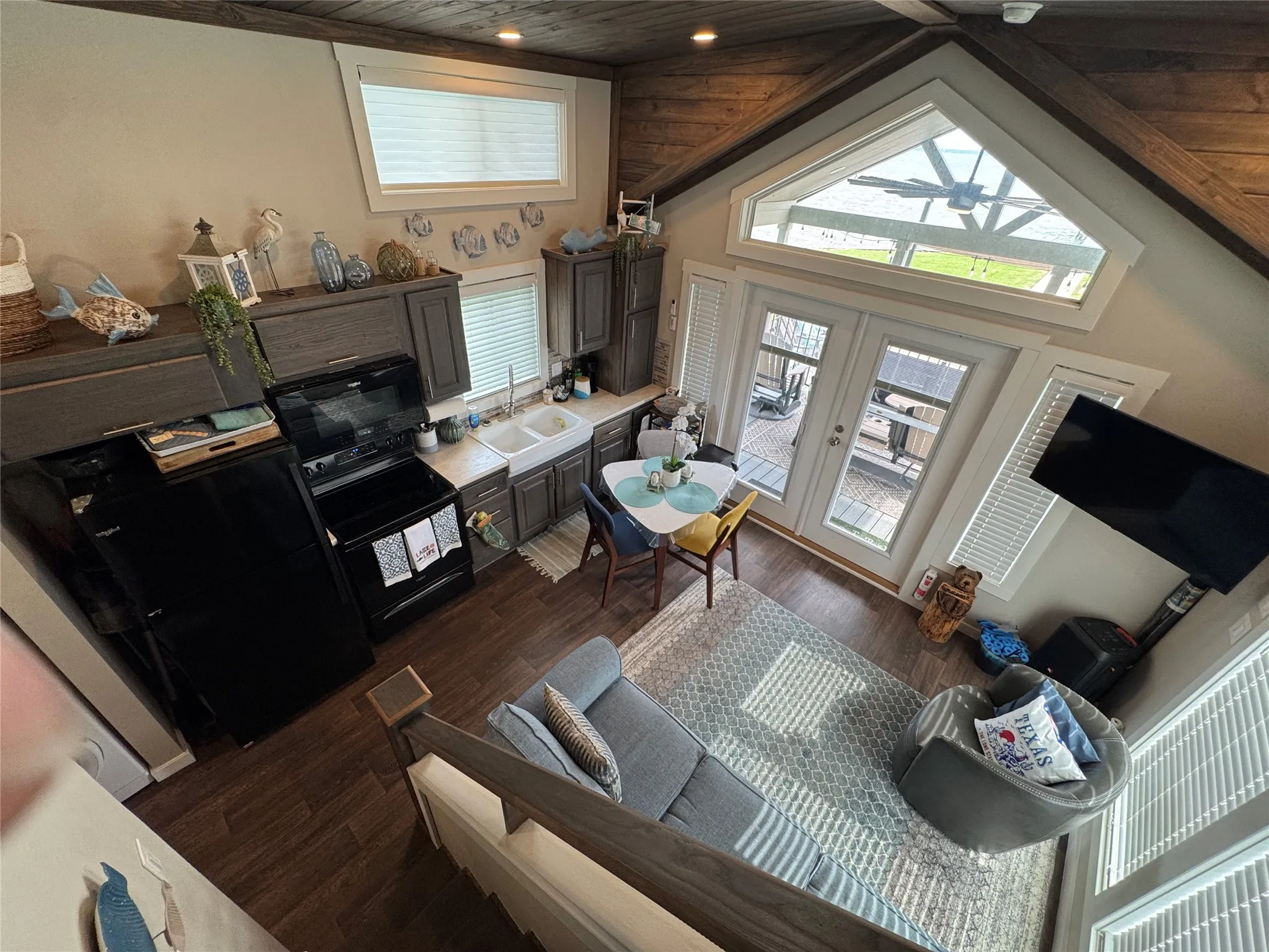 Open-concept living space featuring wood-finish flooring, a vaulted ceiling with exposed wood beams, and a full kitchen