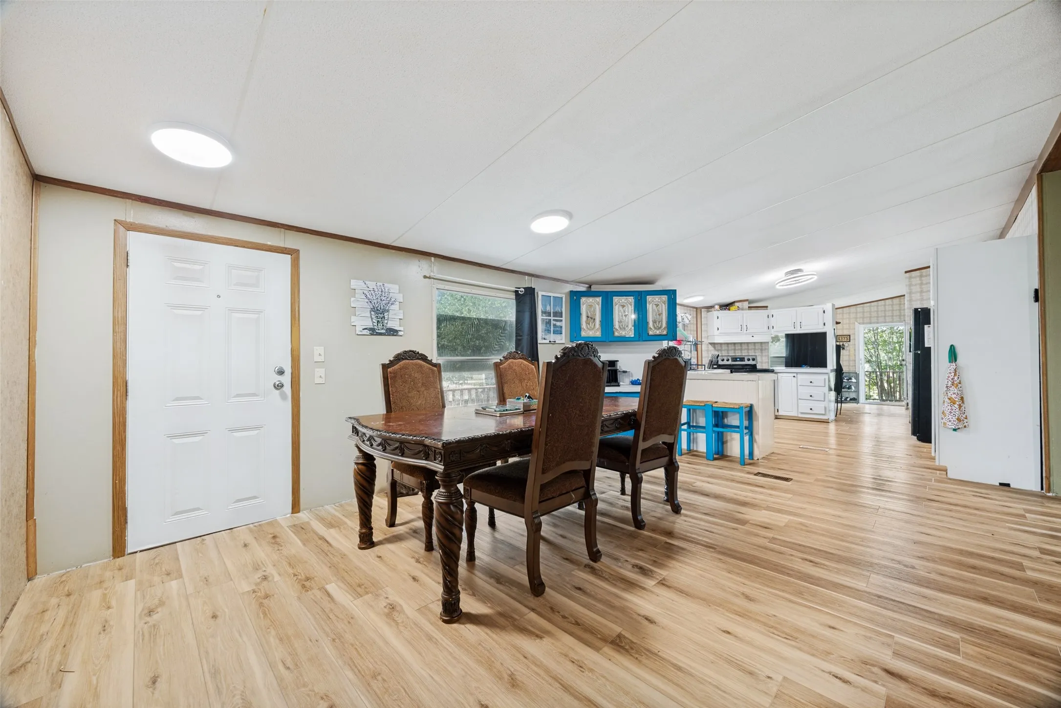 Open-concept interior featuring smooth flooring, windows overlooking front deck, built in buffet and a kitchen with white cabinetry and blue accents.  With a 13x17 footprint, it will support your grandest table.