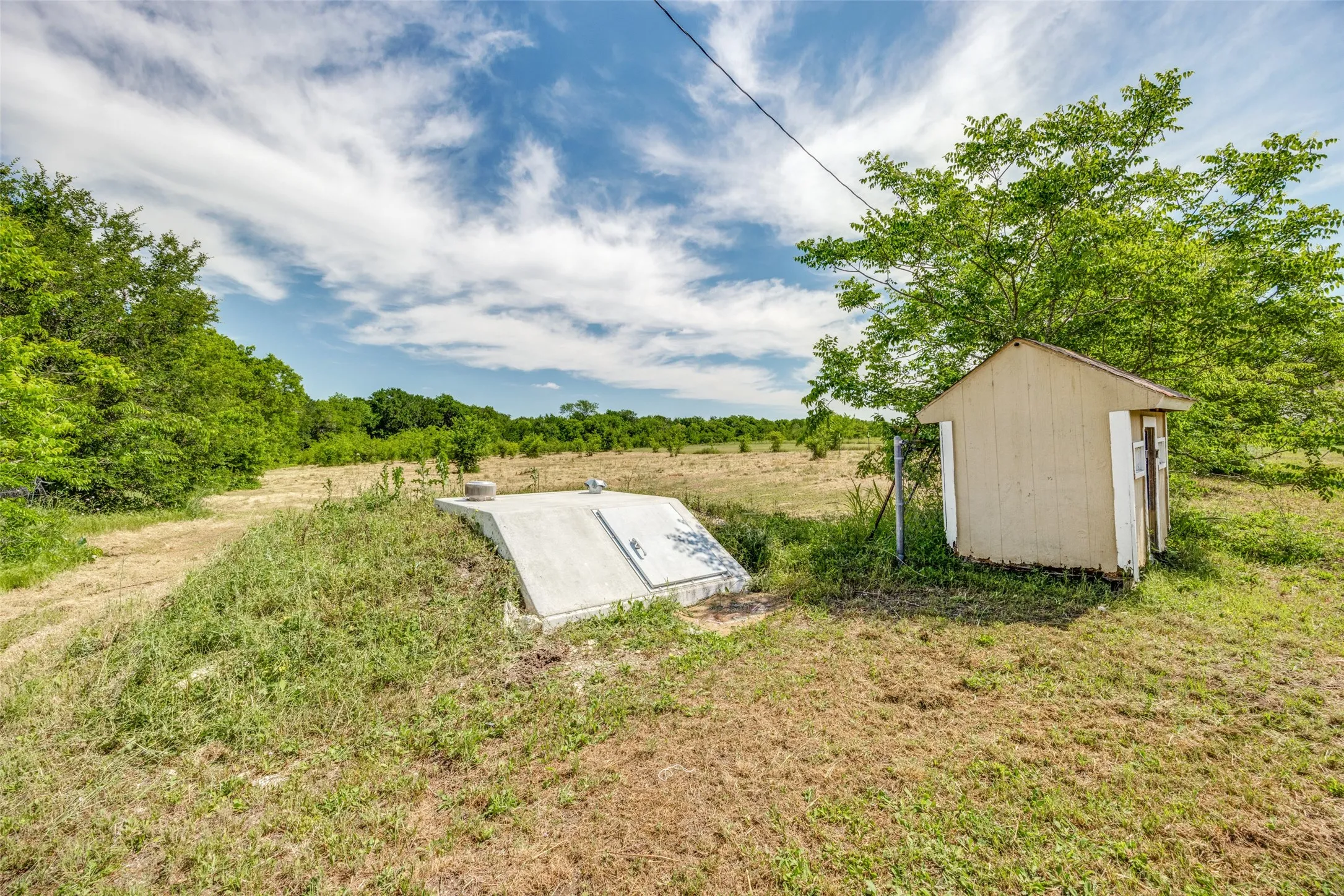 Recently installed Concrete storm shelter with an access hatch and an adjacent small utility shed