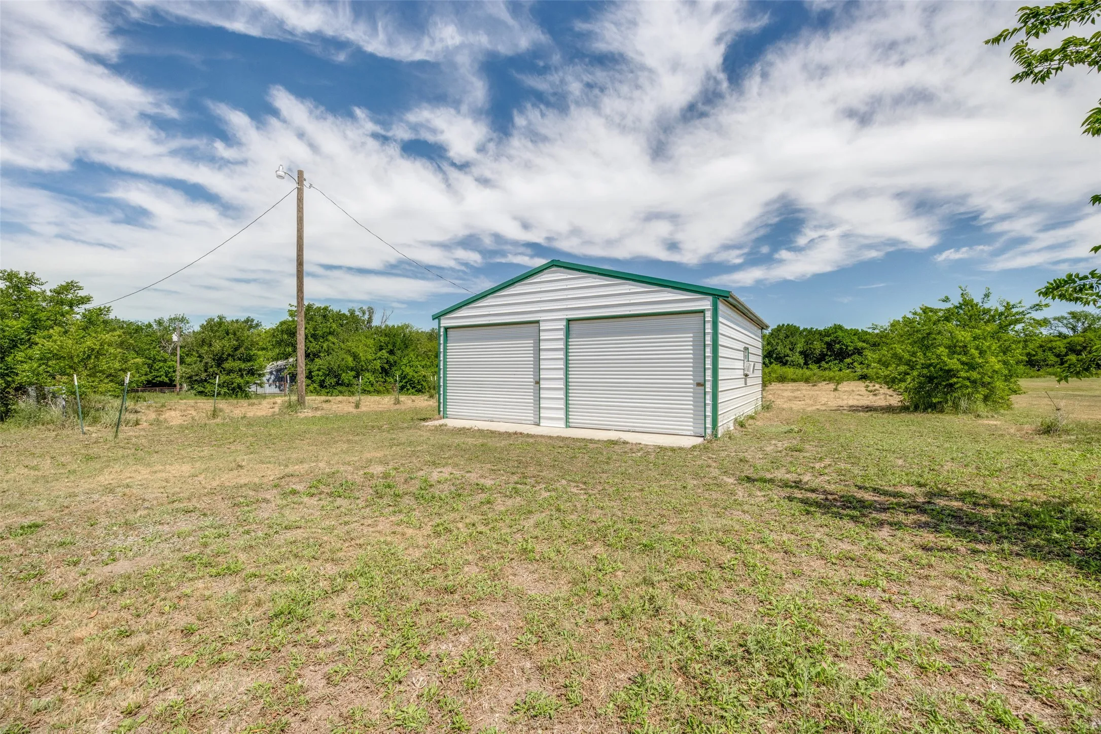 Detached two-bay metal building featuring concrete slab, electricity (separate meter) and even a window AC unity. Shop provides protection for vehicles, extra work & storage area or just a place to hang out.