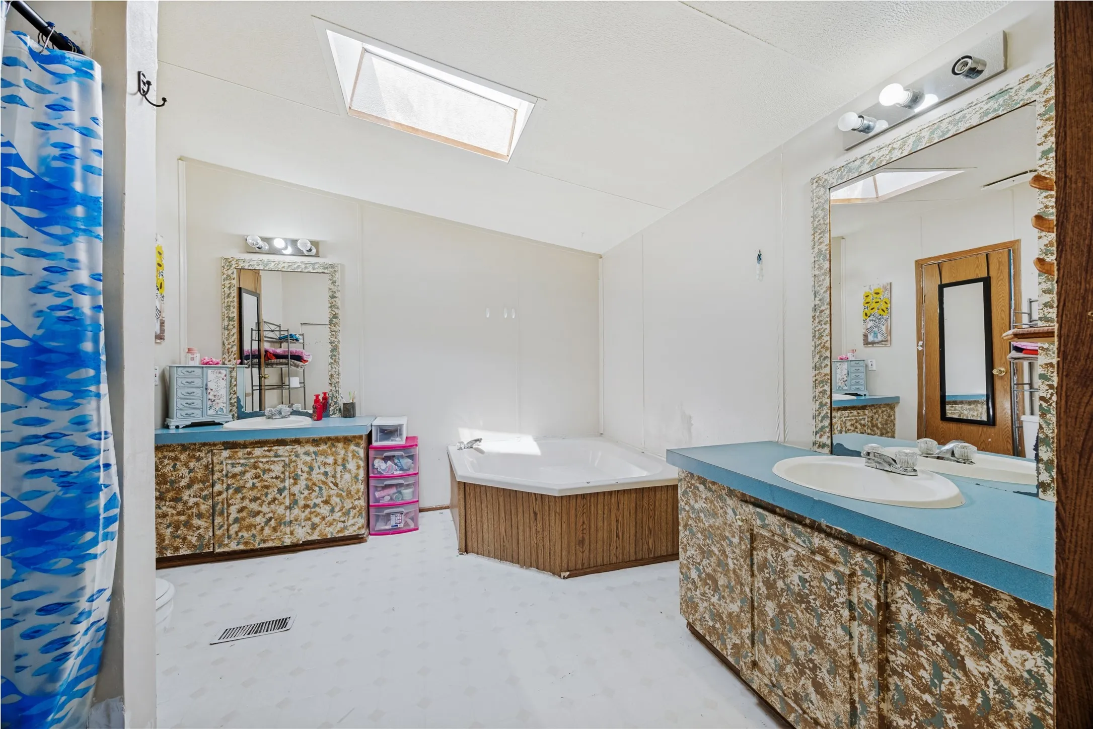En Suite Bathroom featuring a corner soaking tub, dual vanity sinks with camo cabinets & blue countertops, and a skylight. The "camo" custom cabinet paint could stand a fresh coat & updated look.  What will you do?