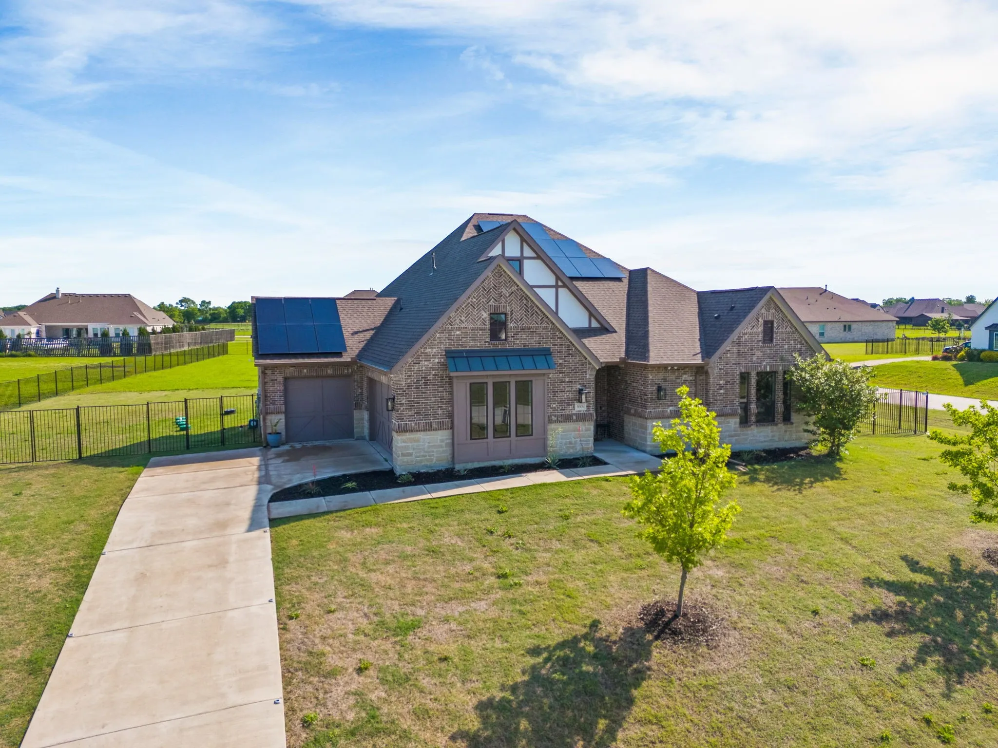 Tudor home with a front lawn, stone siding, roof mounted solar panels, concrete driveway, and fence