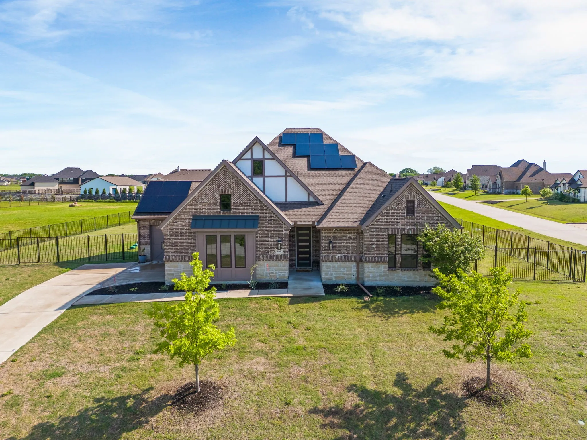 Tudor home featuring roof mounted solar panels, a front yard, fence, and brick siding