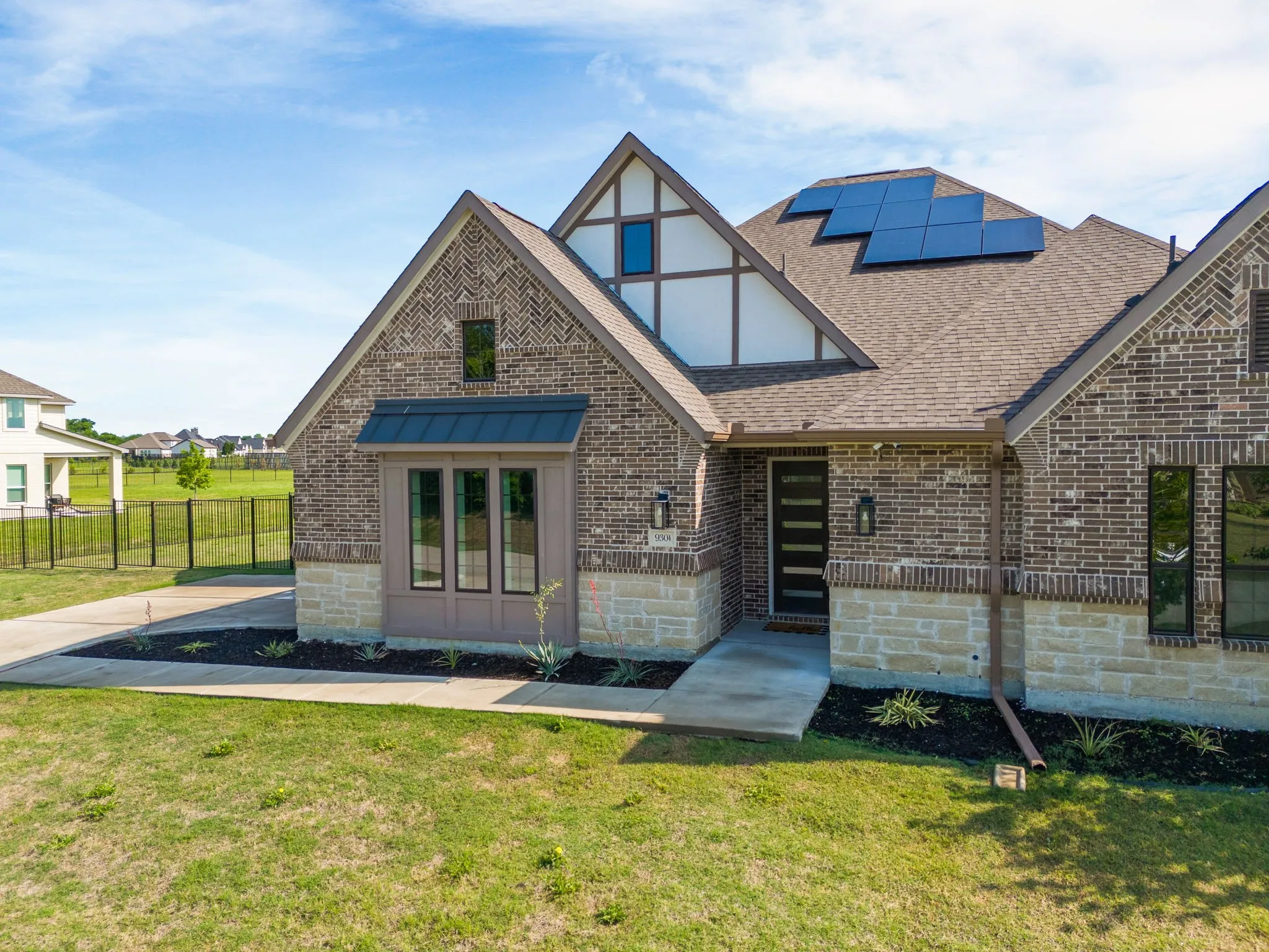 English style home featuring brick siding, solar panels, a front yard, and roof with shingles