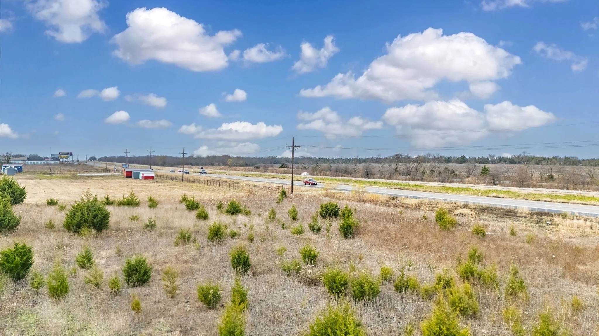 Expansive open acreage featuring varied terrain and natural vegetation, bordered by a multi-lane roadway