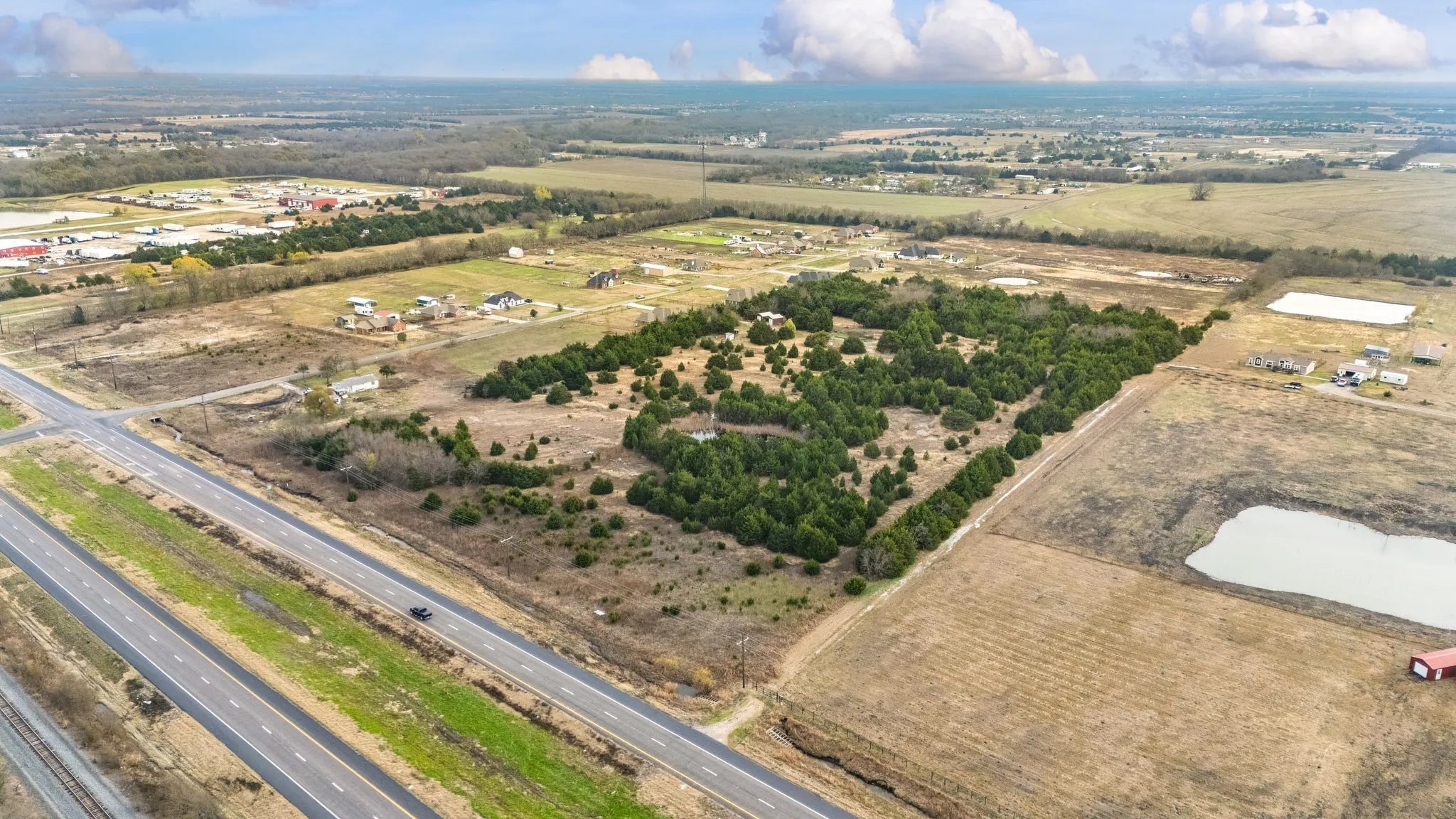 Expansive acreage featuring significant tree coverage, adjacent multi-lane paved roadway, and proximity to additional developed properties
