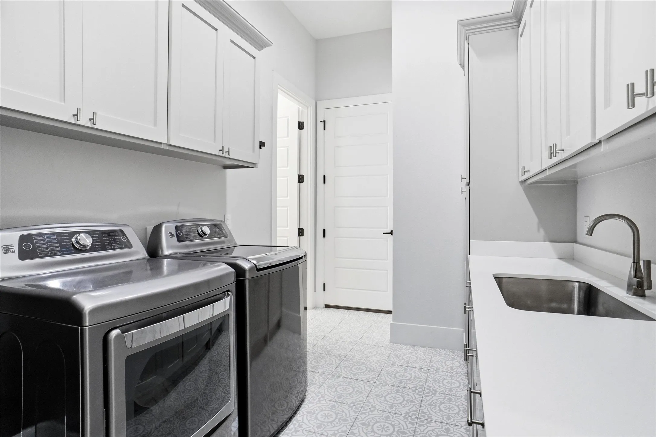 Laundry room featuring patterned tile flooring, white shaker cabinetry, an undermount sink with a gooseneck faucet, and a light countertop