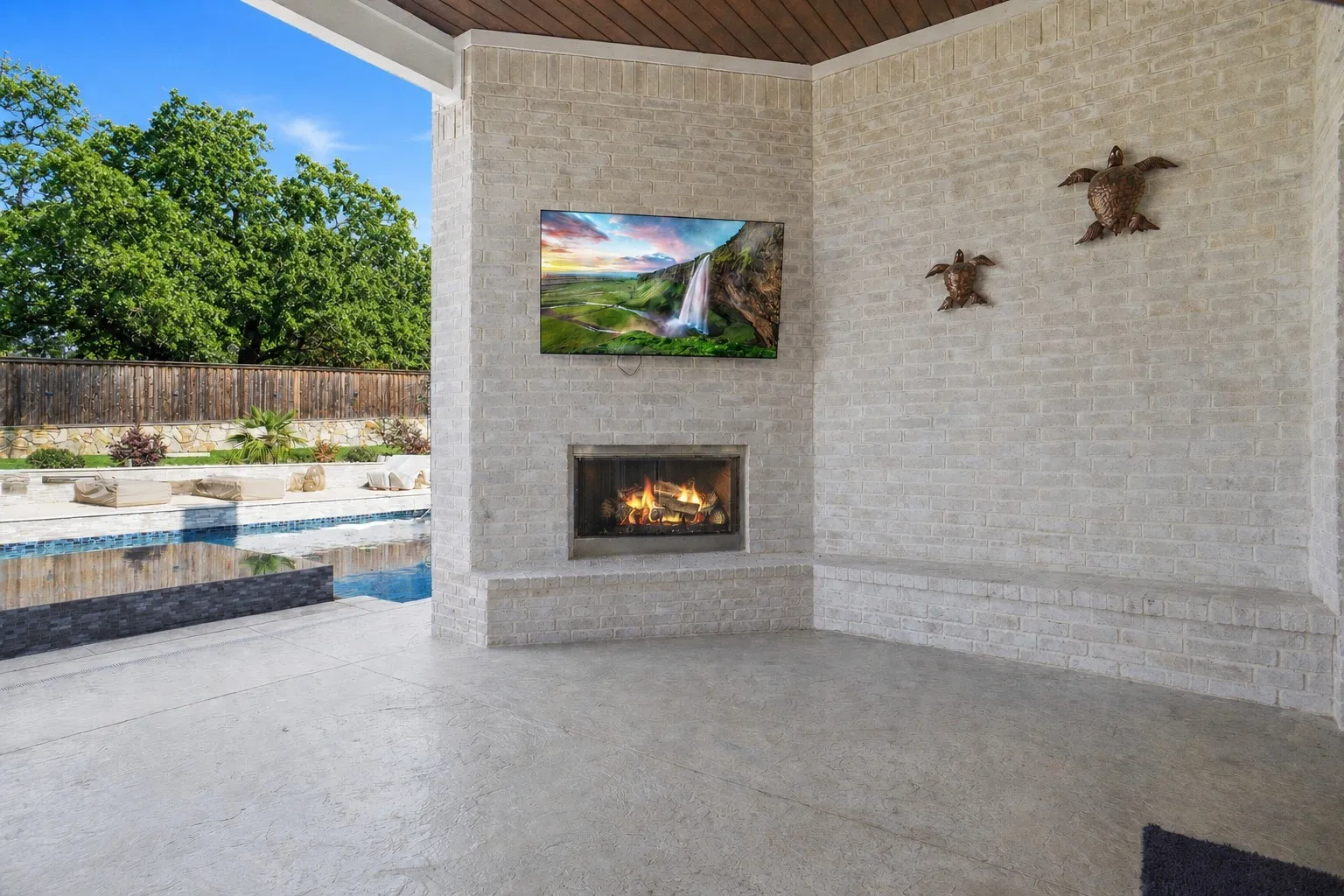 Covered outdoor patio featuring a built-in fireplace, integrated television, and extended brick bench seating