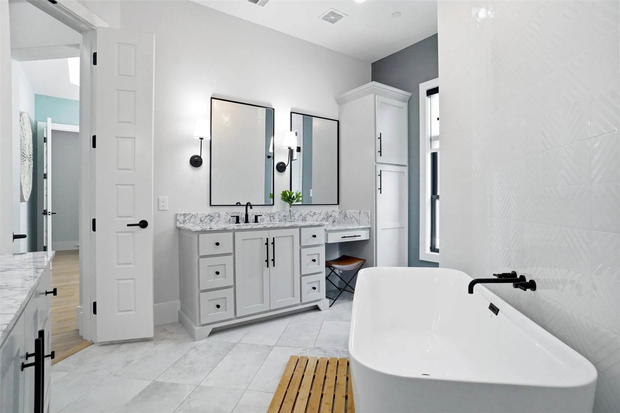 Spacious bathroom featuring a freestanding soaking tub with a wall-mounted faucet, a double vanity with stone countertops, and a built-in storage cabinet