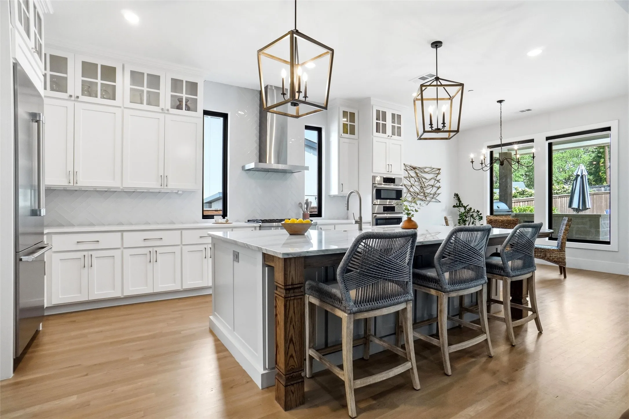 Gourmet kitchen featuring a substantial island with seating, stainless steel appliances, extensive white cabinetry, herringbone tile backsplash, and wood-finish flooring