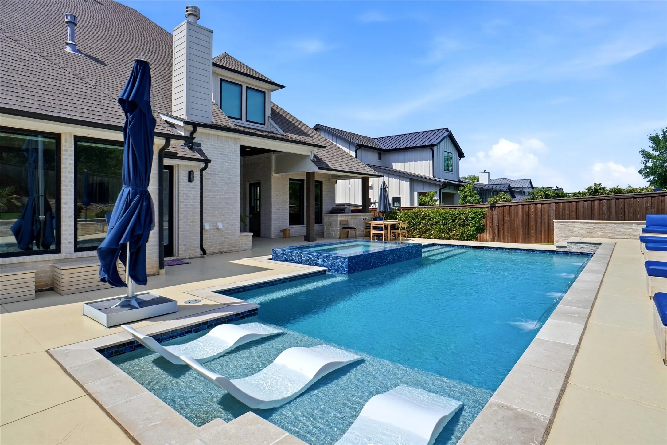 Resort-style pool area featuring a rectangular pool, integrated spa with blue mosaic tile, and a baja shelf with two in-pool loungers