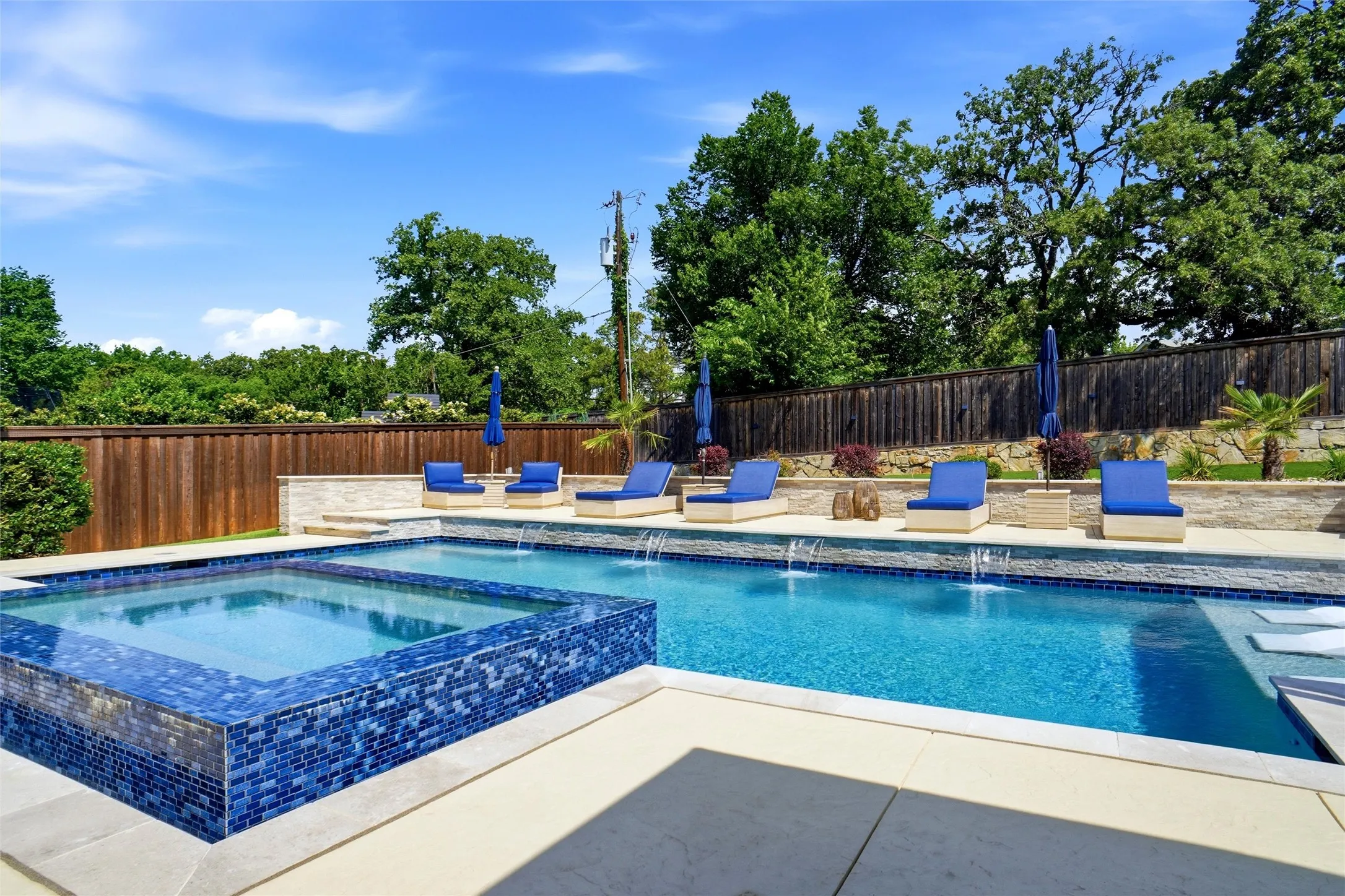 Resort-style pool area featuring a rectangular swimming pool with integrated spa, blue mosaic tile accents, and multiple water features
