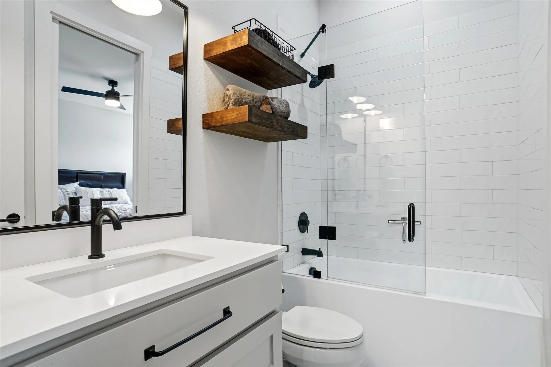 Full bathroom featuring a white vanity with an integrated sink, matte black fixtures, a framed mirror, and a tiled tub/shower combination with a glass enclosure