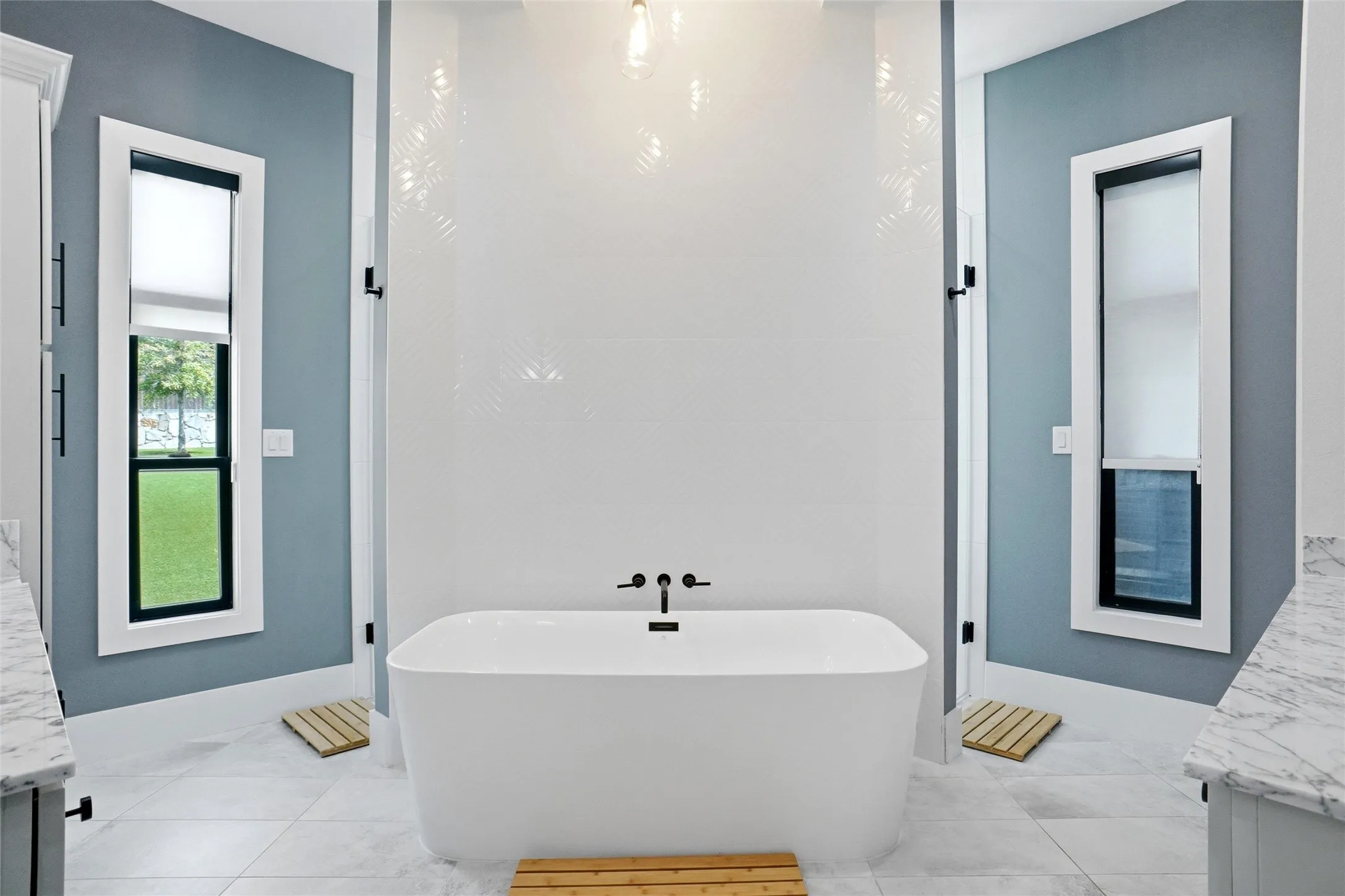 Freestanding soaking tub with matte black fixtures, set against a textured white tile wall