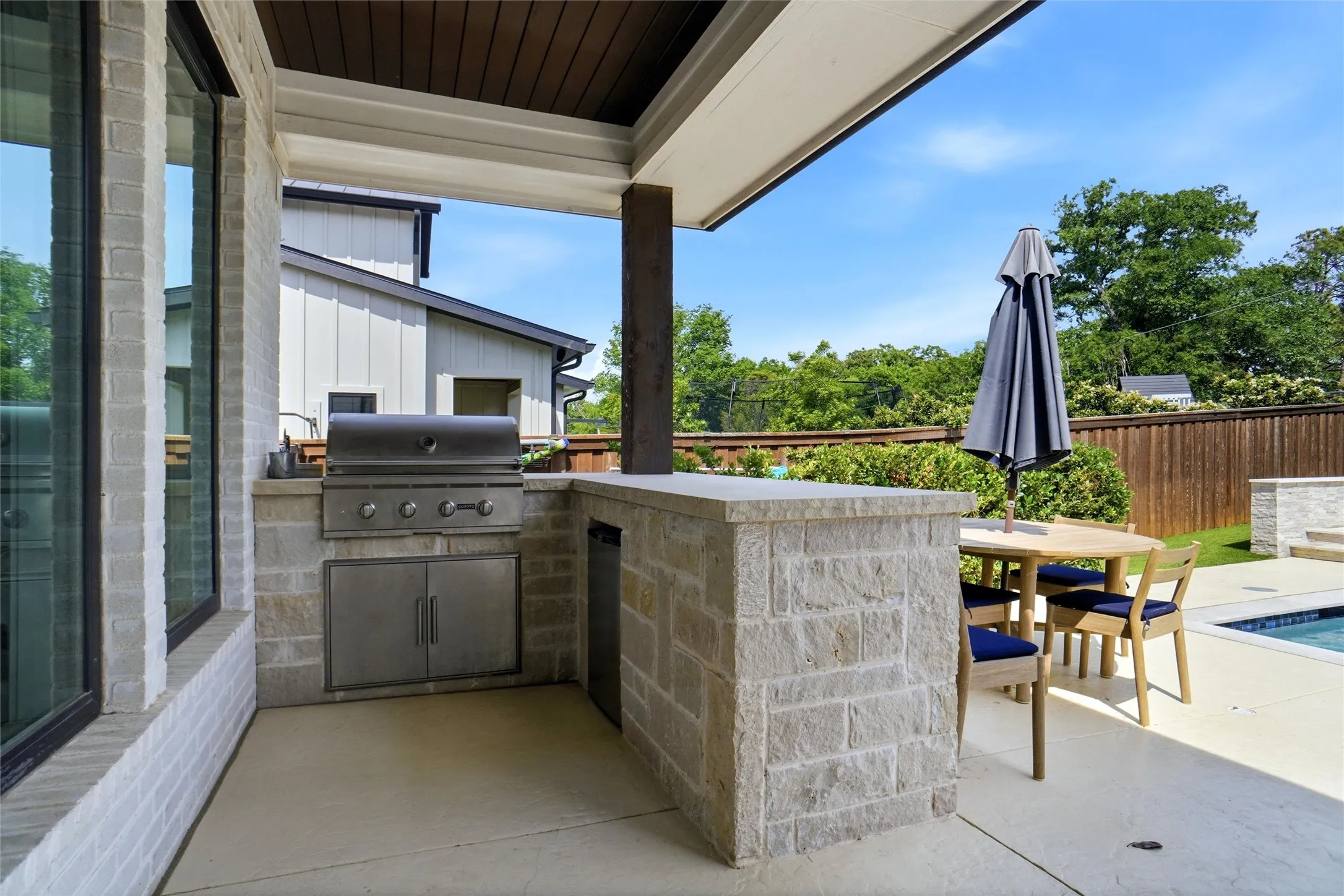 Covered outdoor living space featuring an integrated grill station with stainless steel appliances and stone block construction