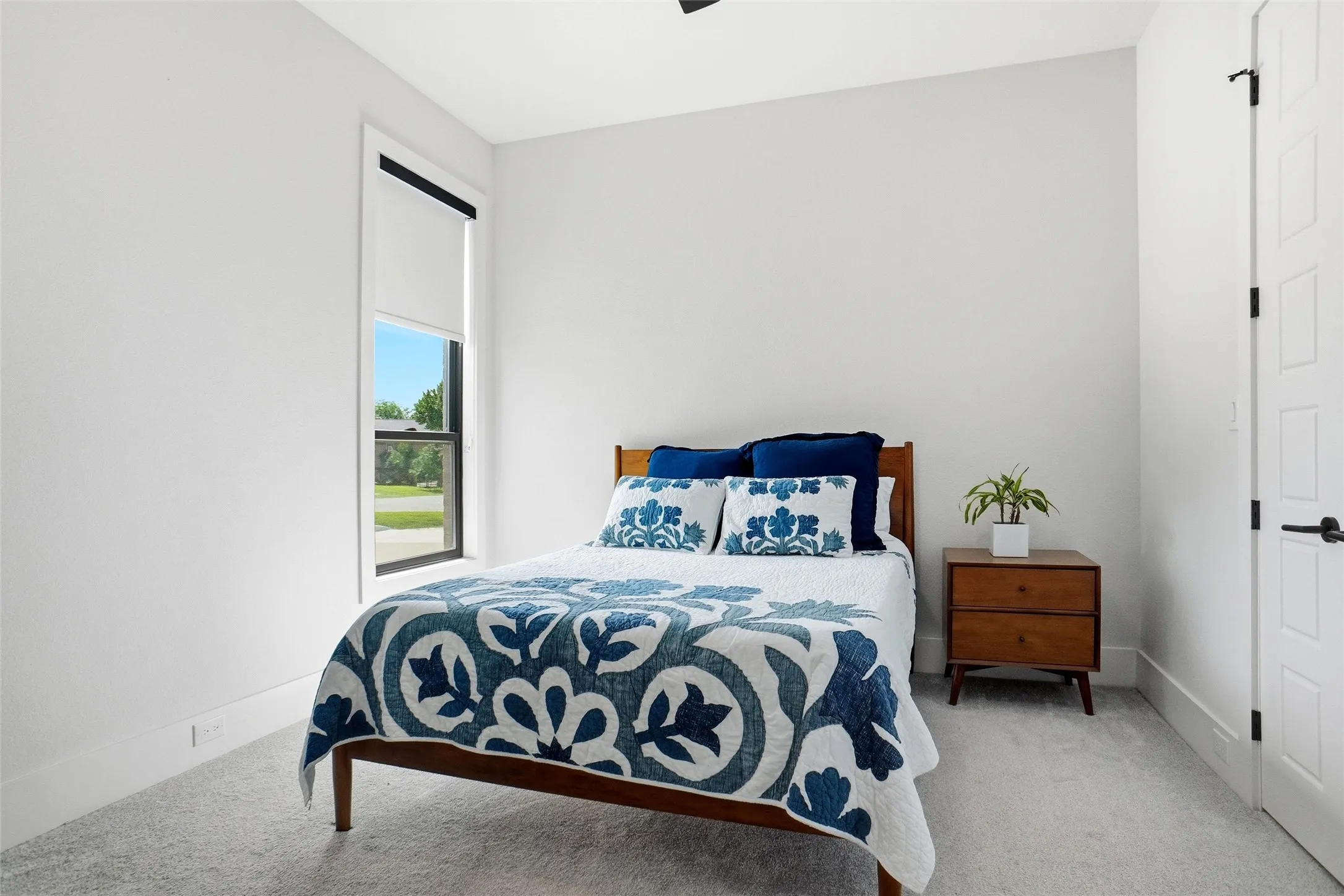 Interior room with light gray carpeting, white walls, and a single window featuring a roller shade and black trim