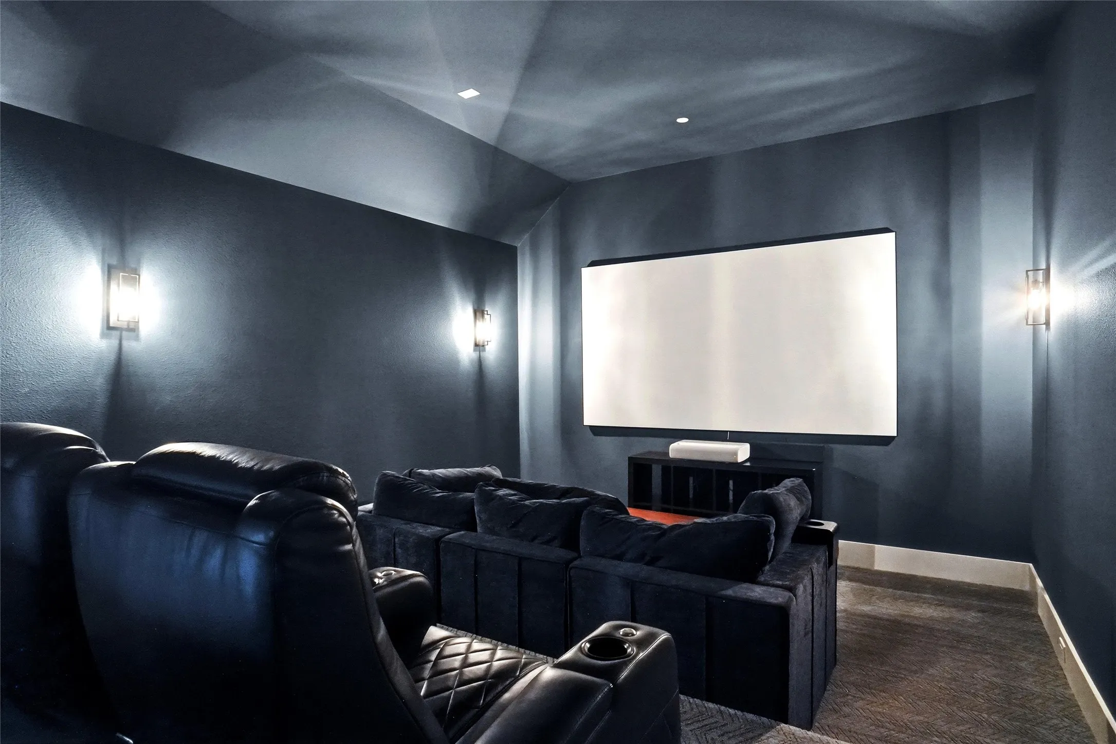 Dedicated media room featuring a large projection screen, built-in media console, and wall-mounted sconce lighting