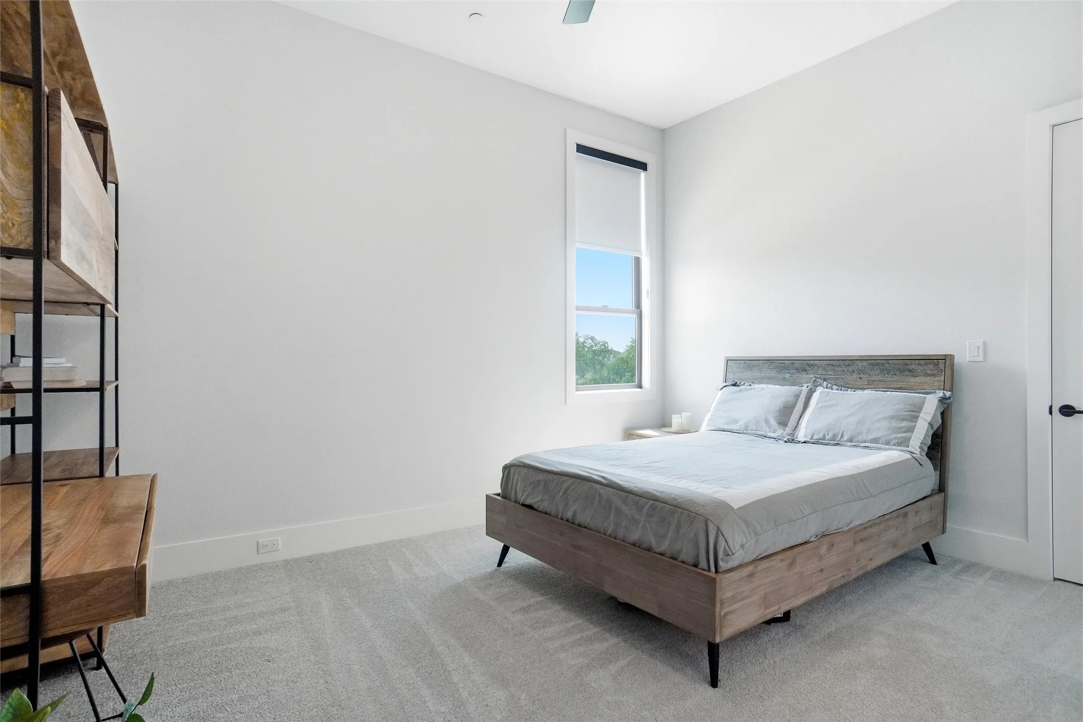 Carpeted room featuring a single window with a roller shade, white walls, and a ceiling fan