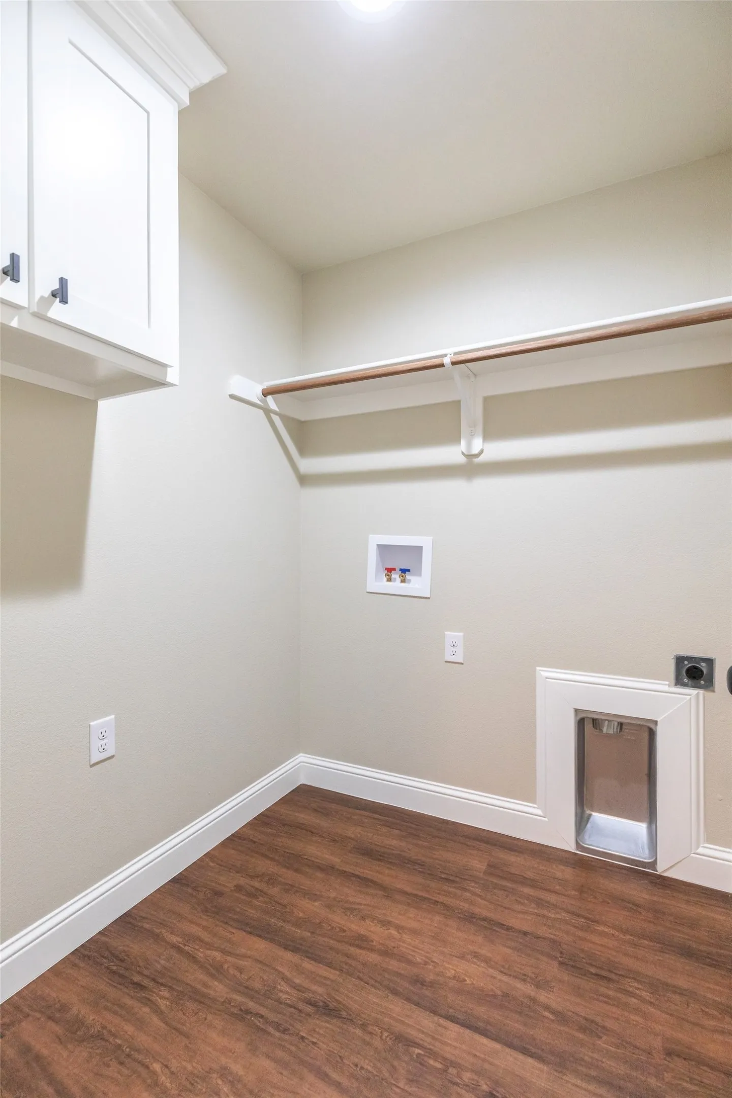 Laundry room with wood-finish flooring, light neutral wall paint, white baseboards, and overhead white cabinetry with dark hardware