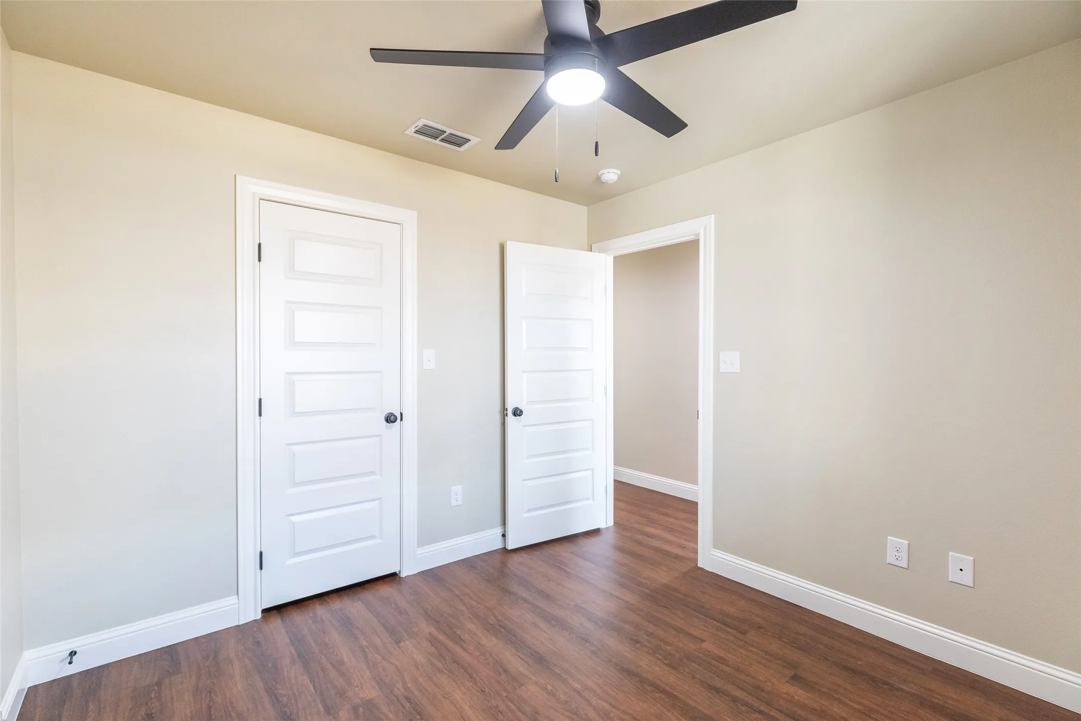 Room featuring wood-finish flooring, light-toned walls, white trim, white panel doors, and a ceiling fan with integrated lighting