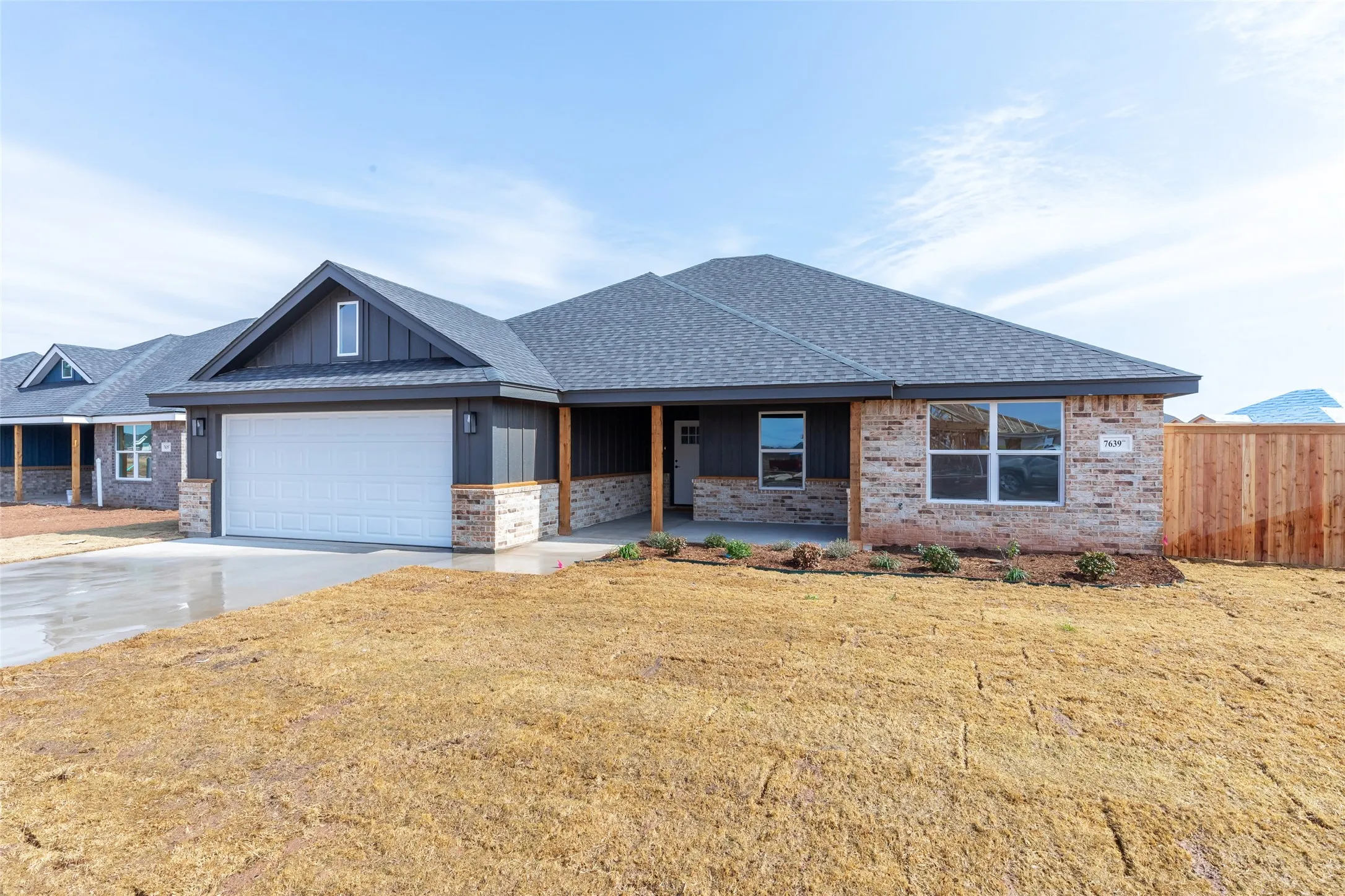 Contemporary ranch-style home featuring a dark gray vertical siding and light-toned brick facade