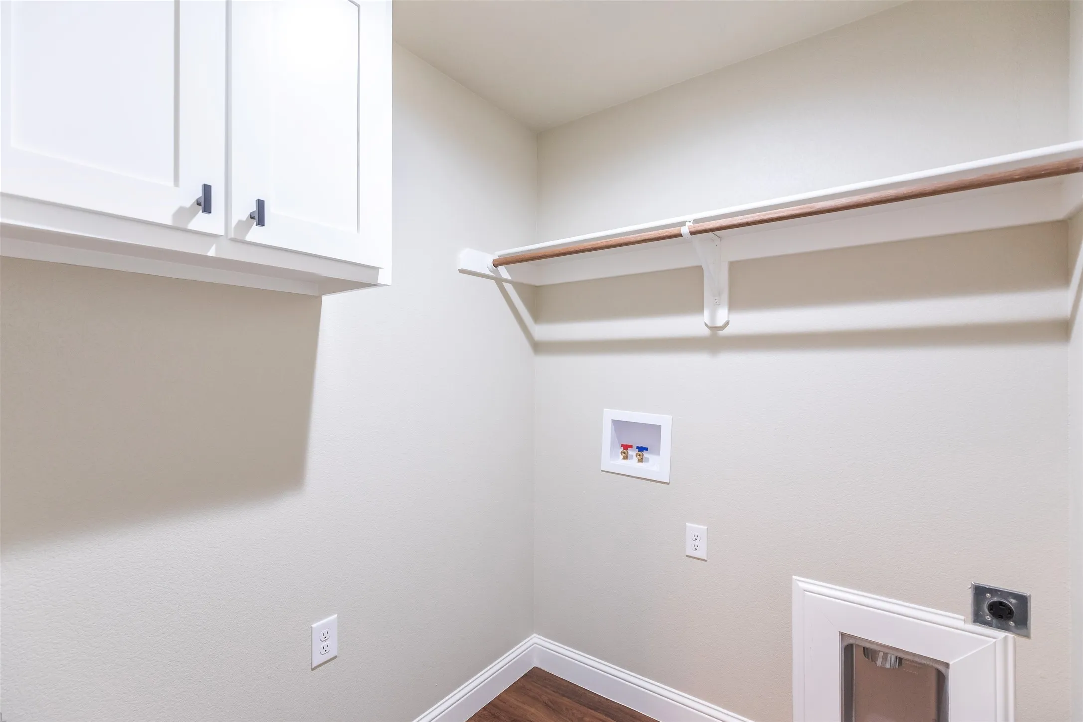 Utility area featuring white shaker-style cabinetry with matte black hardware, a wooden clothes rod, and wood-finish flooring