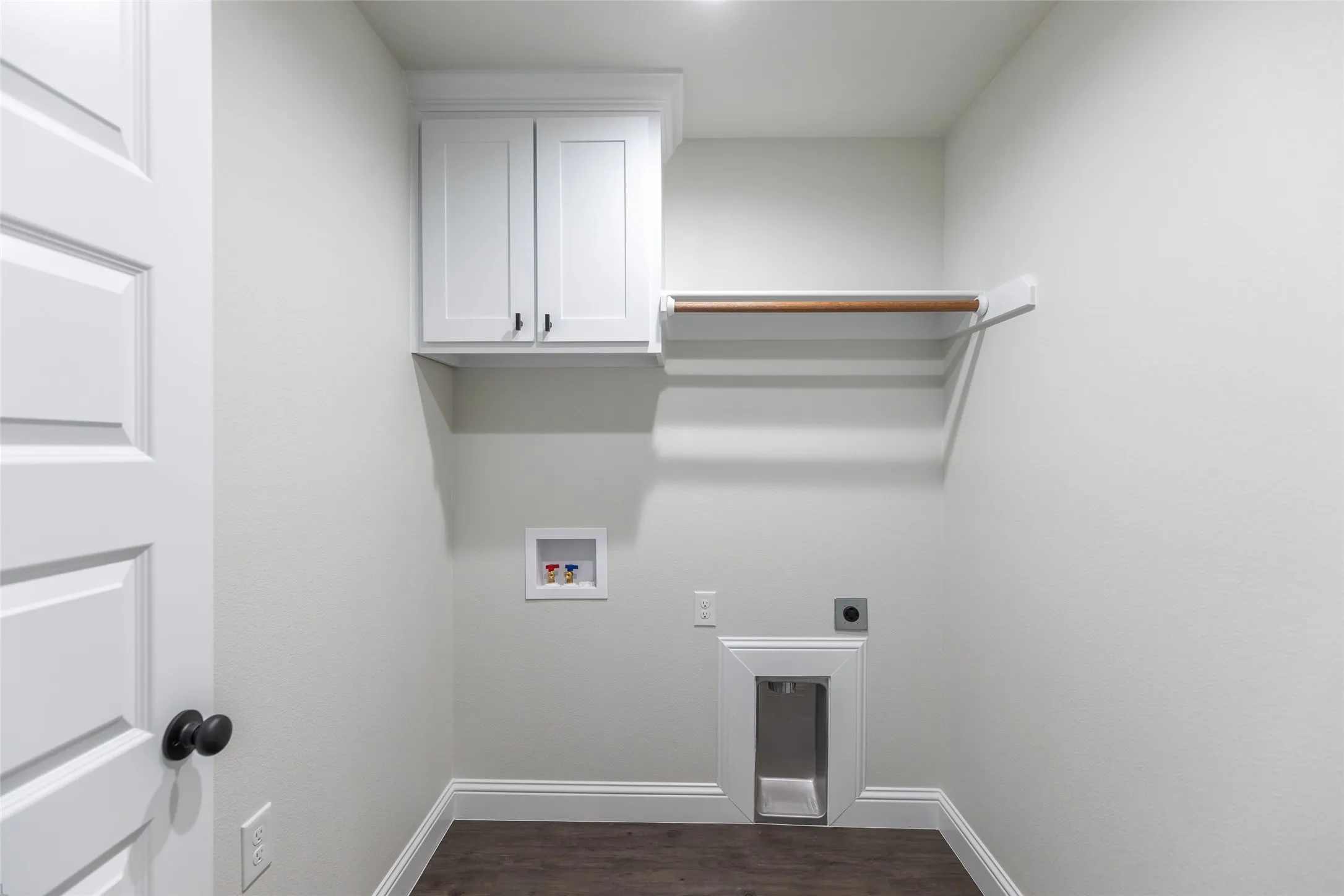 Dedicated laundry area featuring a white shaker-style cabinet, a wood hanging rod, dark wood-finish flooring, and crisp white baseboards