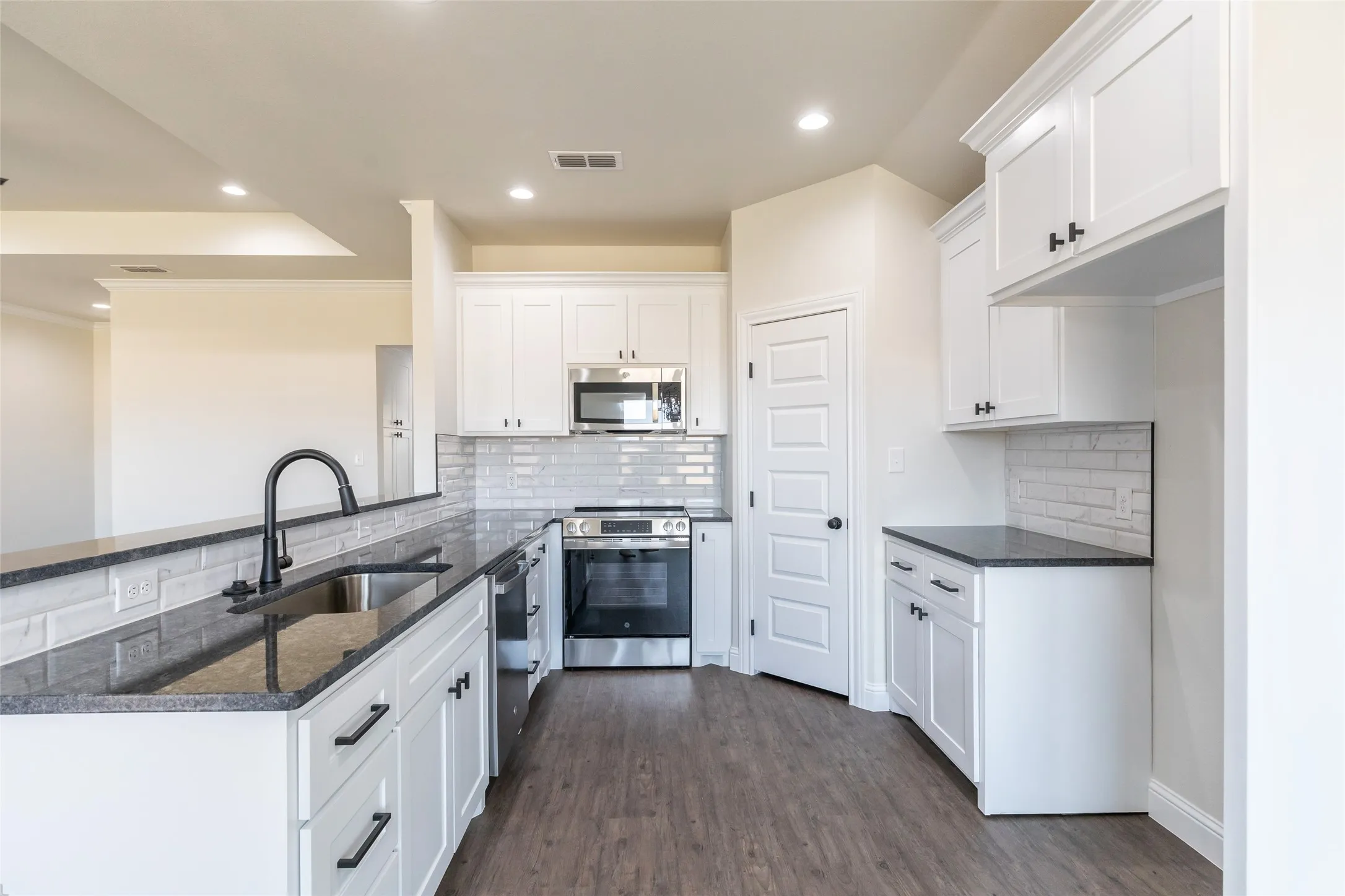 Modern kitchen featuring white shaker cabinetry, dark granite-style countertops, a subway tile backsplash, stainless steel appliances, and wood-finish flooring