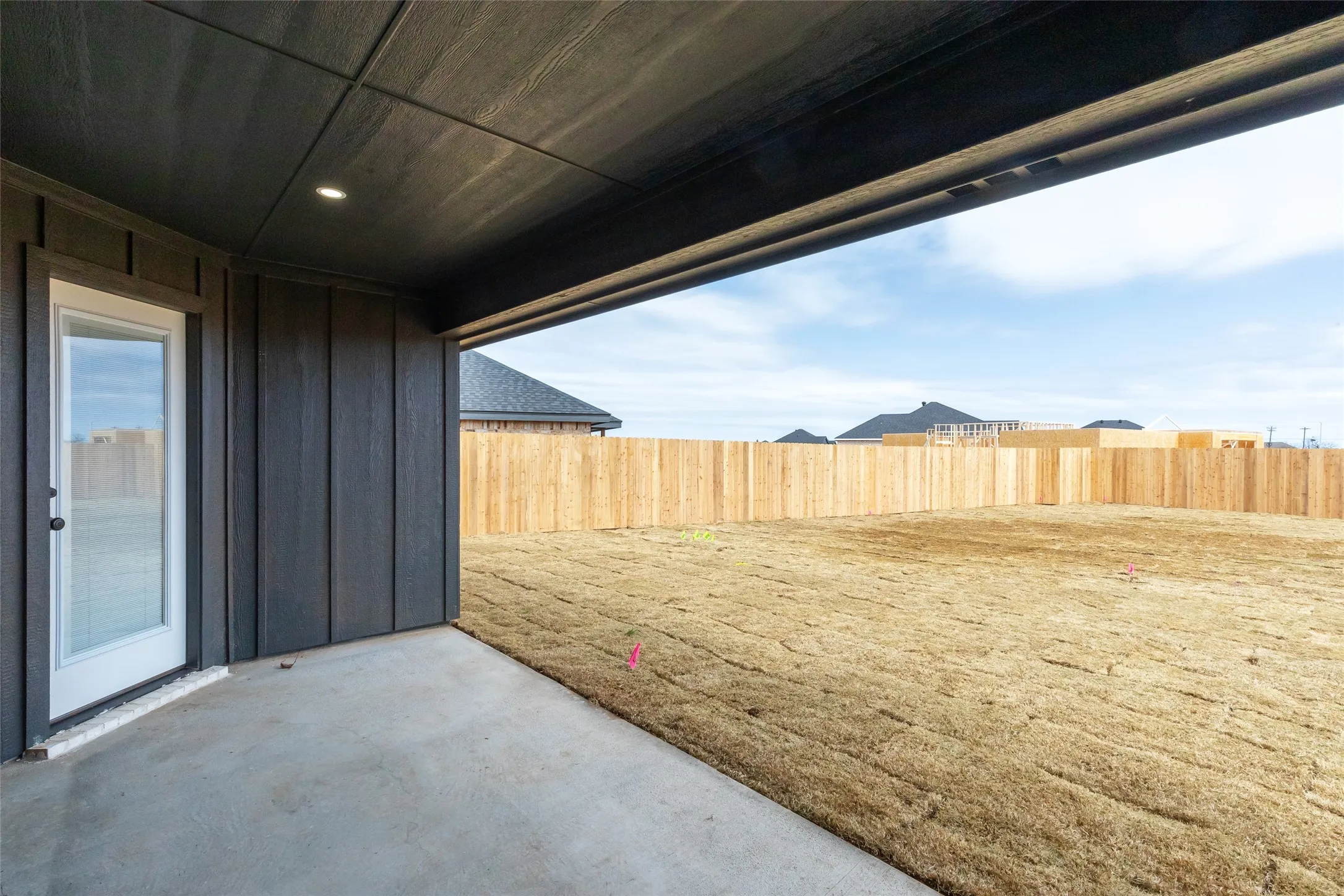 Covered patio with a concrete surface, featuring dark vertical siding and recessed lighting