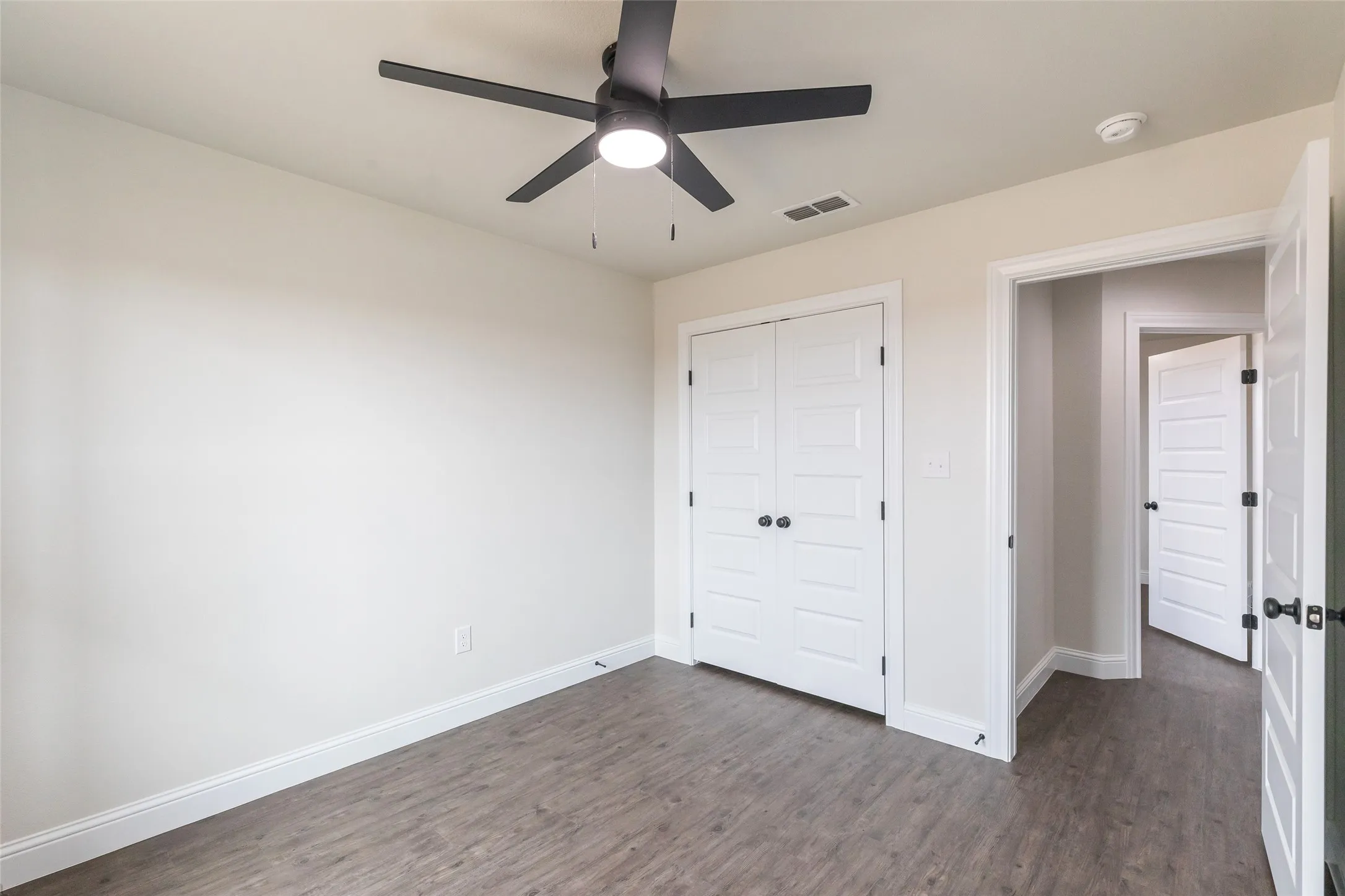 Room featuring wood-finish flooring, a contemporary black ceiling fan with integrated lighting, white baseboards, and a double-door closet with black hardware
