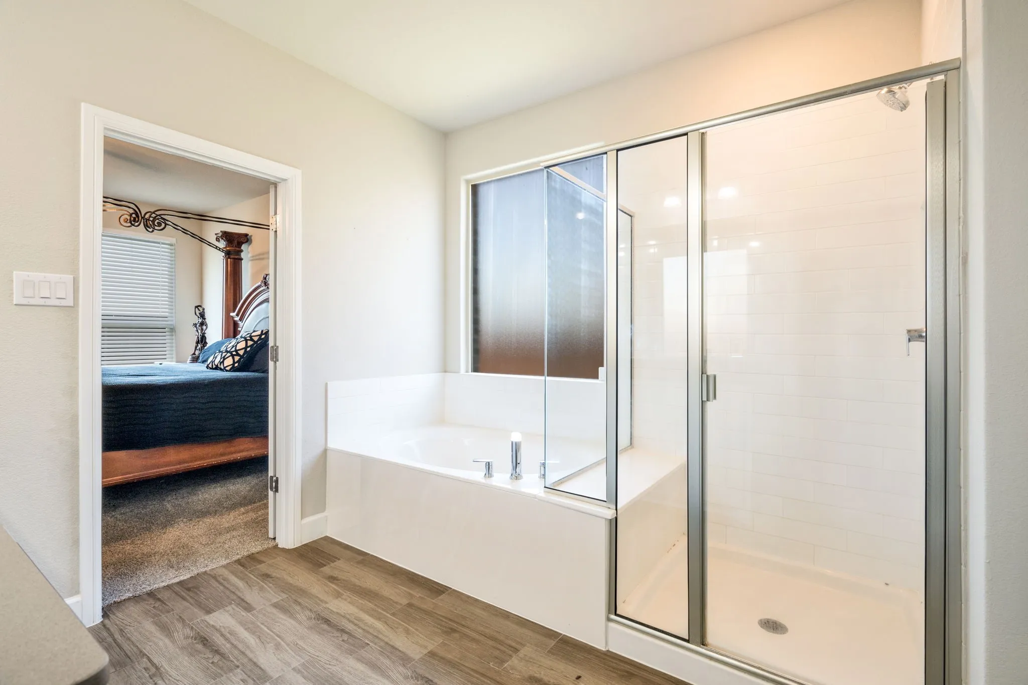 Bathroom featuring wood-finish flooring, a built-in soaking tub, and a separate glass-enclosed shower with white subway tile