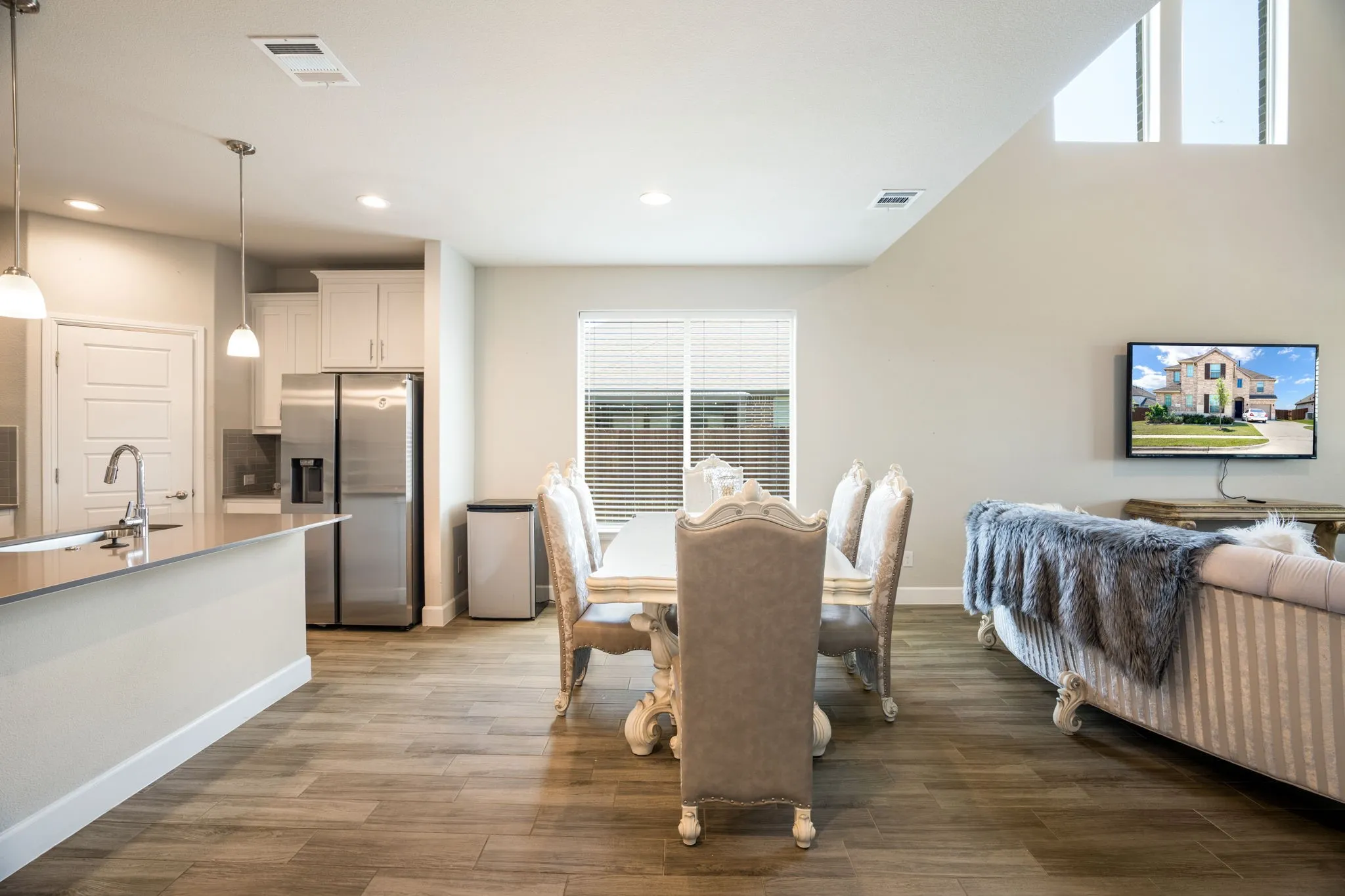 Open-concept living space featuring wood-finish flooring, a kitchen island with pendant lighting, stainless steel appliances, a vaulted ceiling with high windows, and recessed lighting