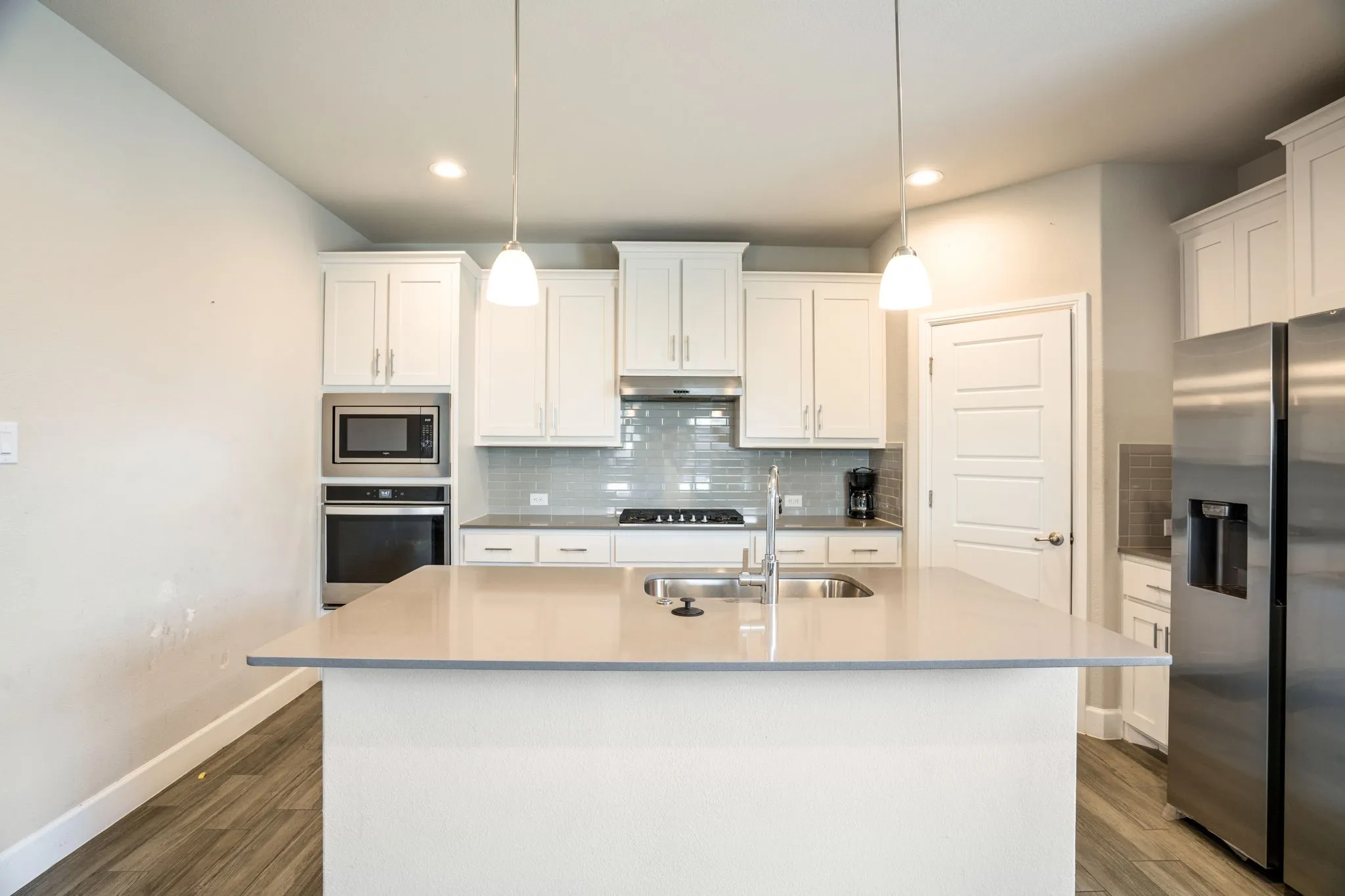 Kitchen featuring a large island with sink, stainless steel appliances, built-in oven and microwave, white shaker-style cabinetry, and wood-finish flooring