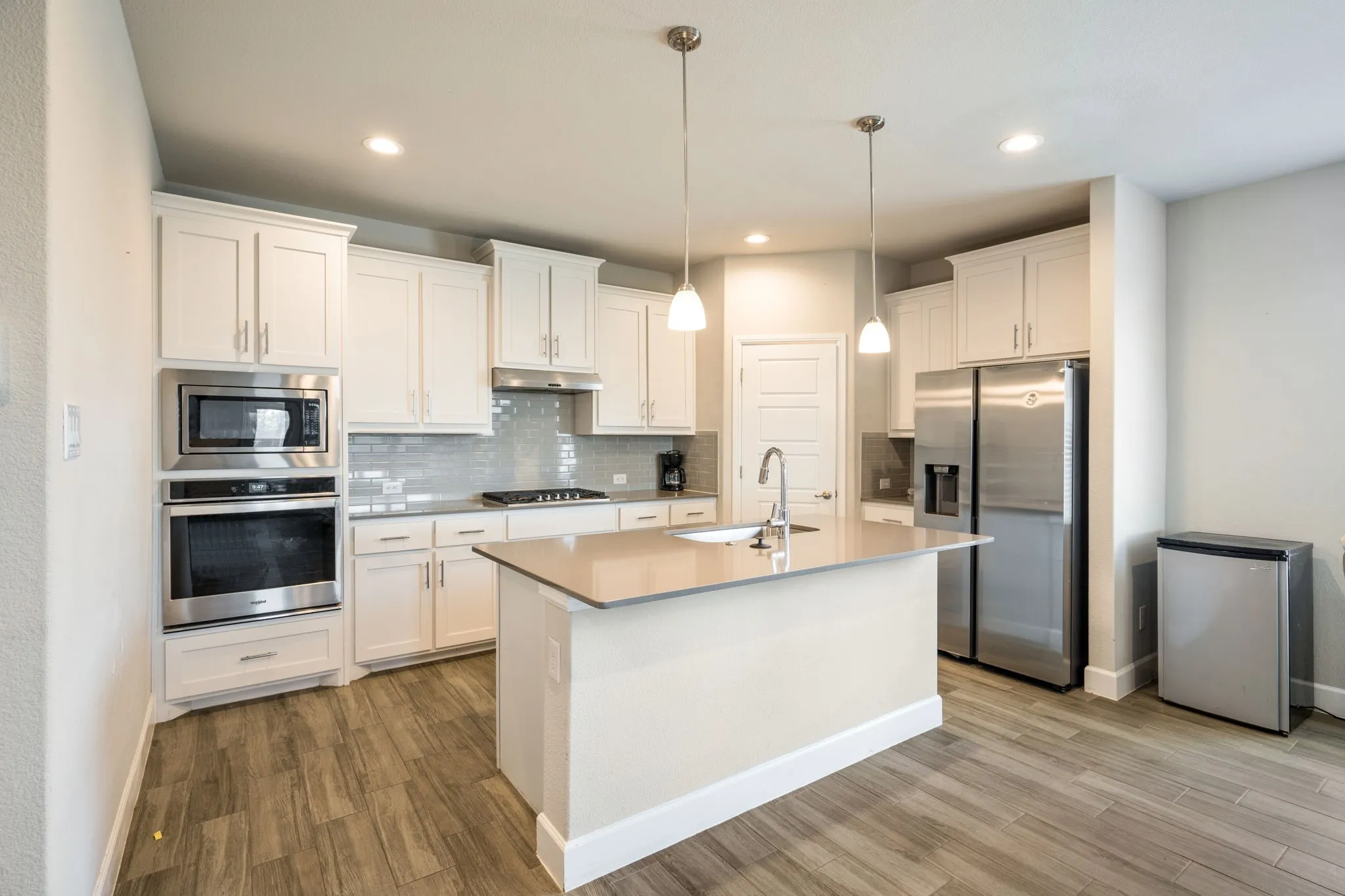 Modern kitchen featuring light wood-finish flooring, white cabinetry, stainless steel appliances, and a central island with a sink and pendant lighting