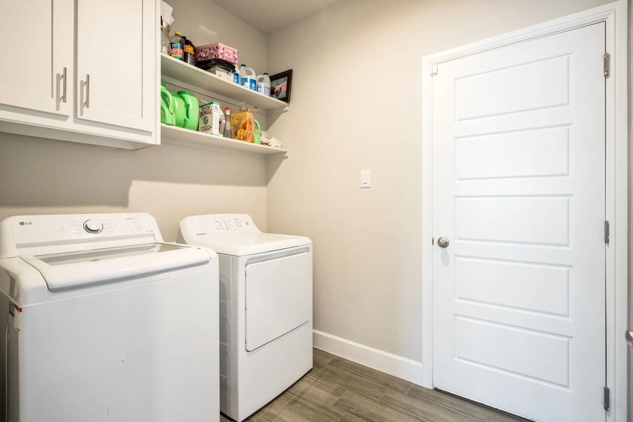 Laundry area featuring white cabinetry, open shelving, and wood-finish flooring