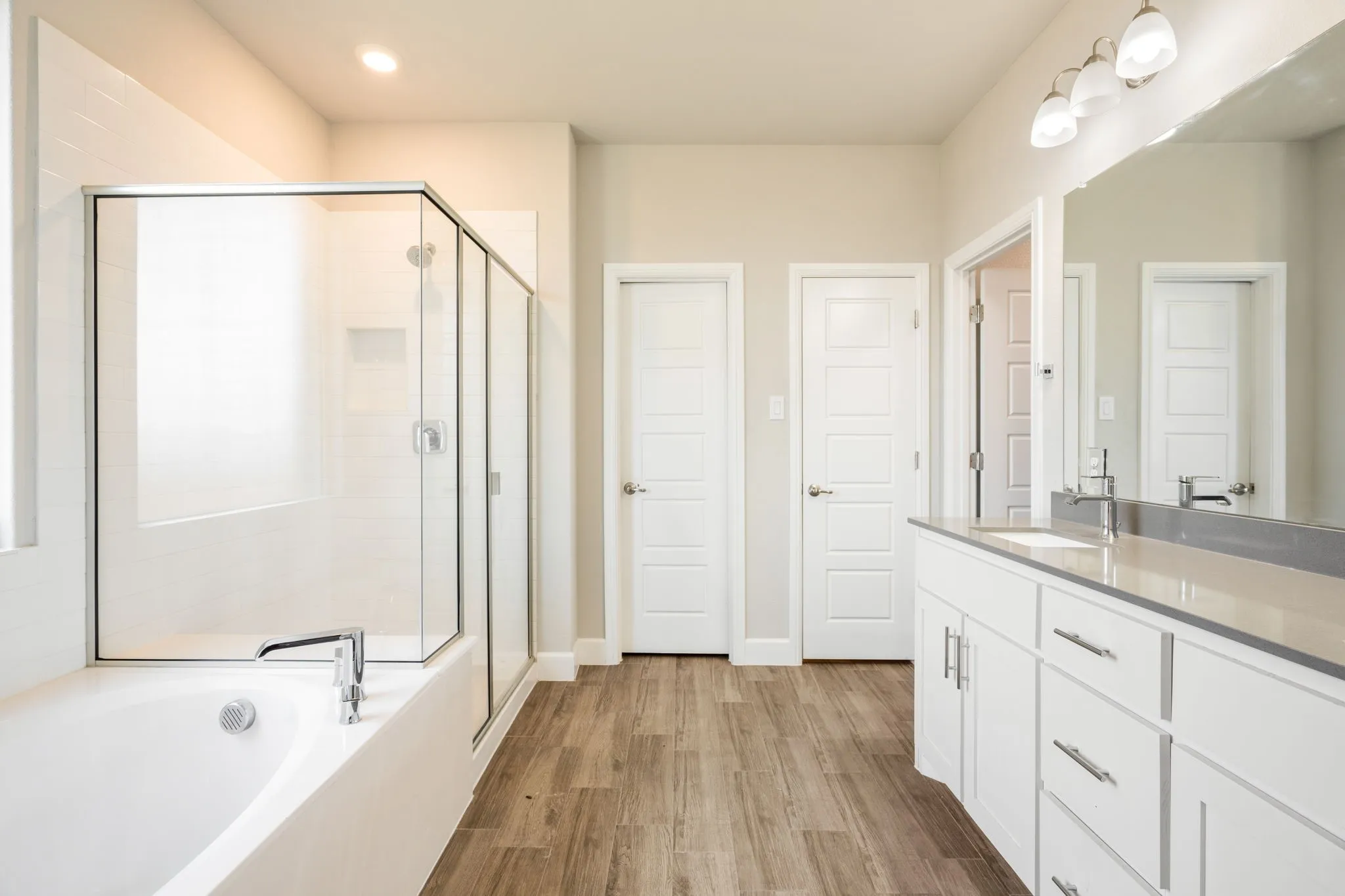 Bathroom featuring a soaking tub, glass-enclosed shower, dual vanity with undermount sinks, and wood-finish flooring
