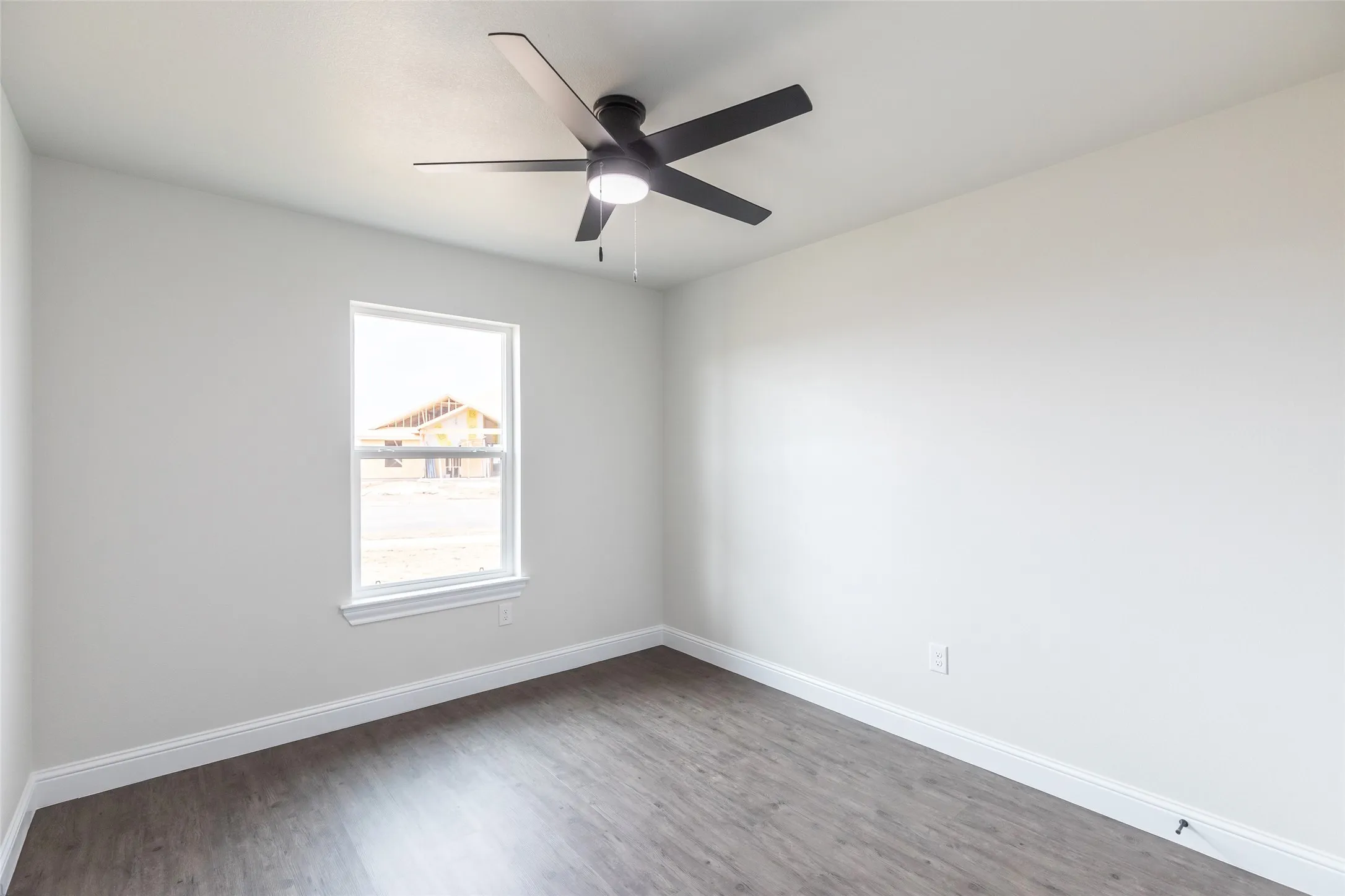 Spacious room featuring wood-finish flooring, white baseboards, and a contemporary black ceiling fan with integrated lighting