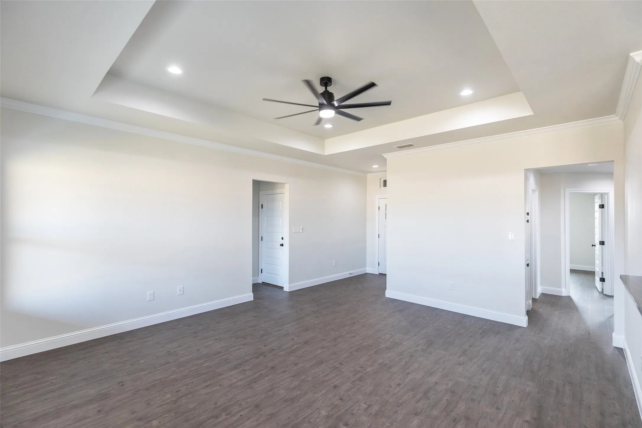 Tray ceiling with recessed lighting and a ceiling fan, wood-finish flooring, white baseboards, and white paneled doors