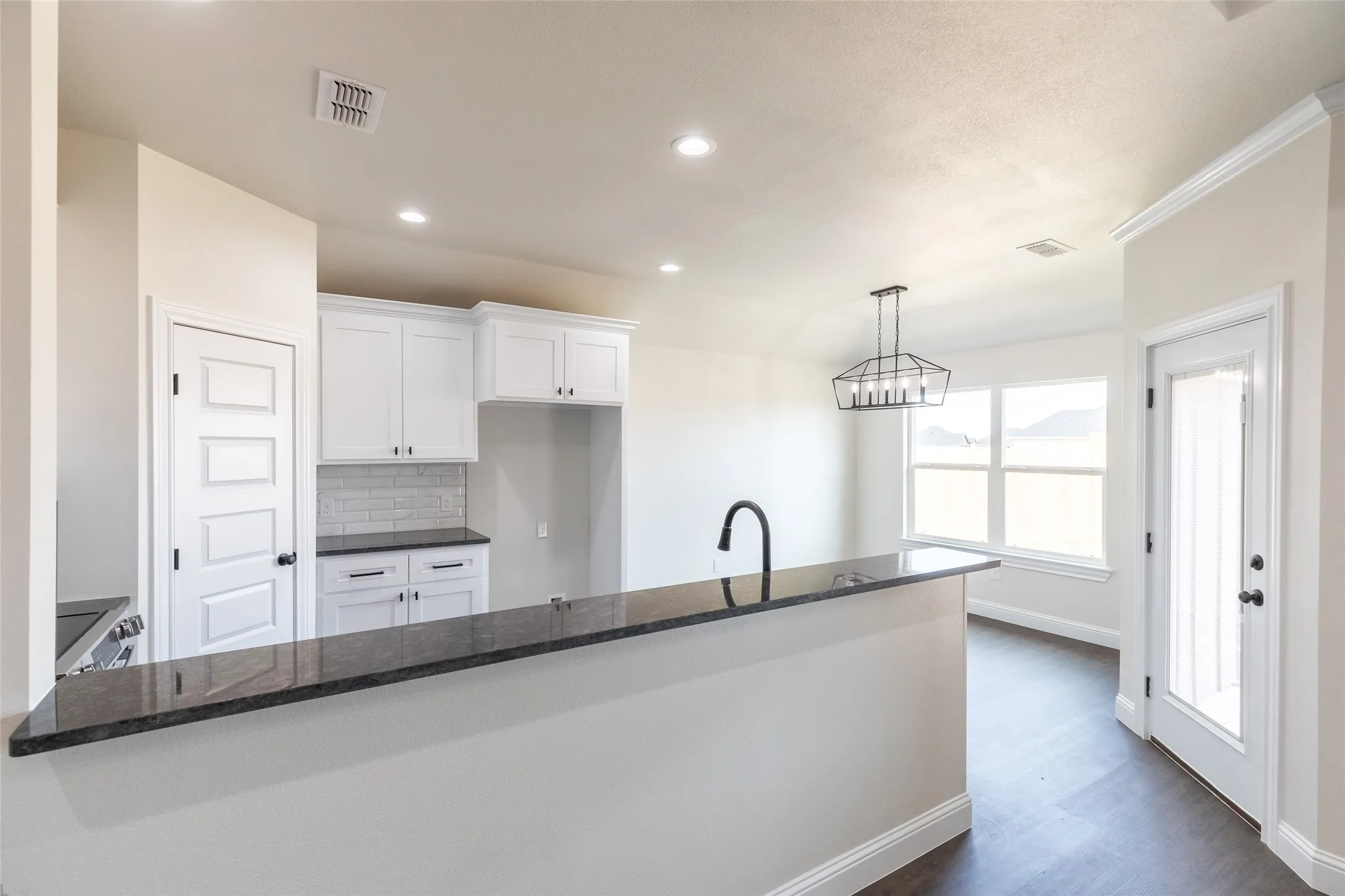 Kitchen featuring a breakfast bar with dark countertops, white cabinetry, subway tile backsplash, and a modern pendant light fixture