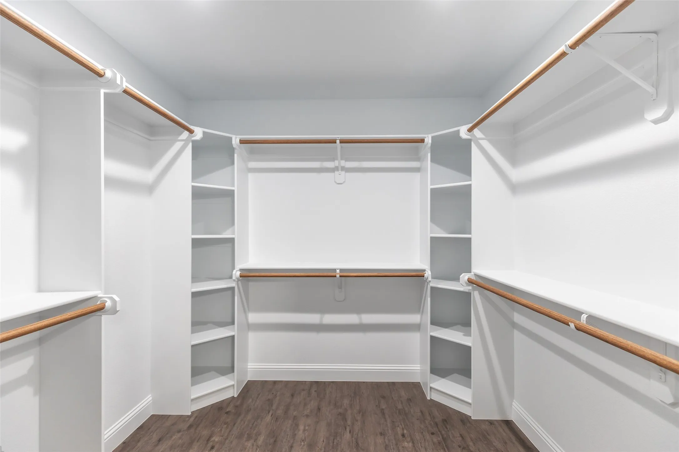 Walk-in closet featuring wood-finish flooring, white built-in shelving, white baseboards, and multiple hanging rods