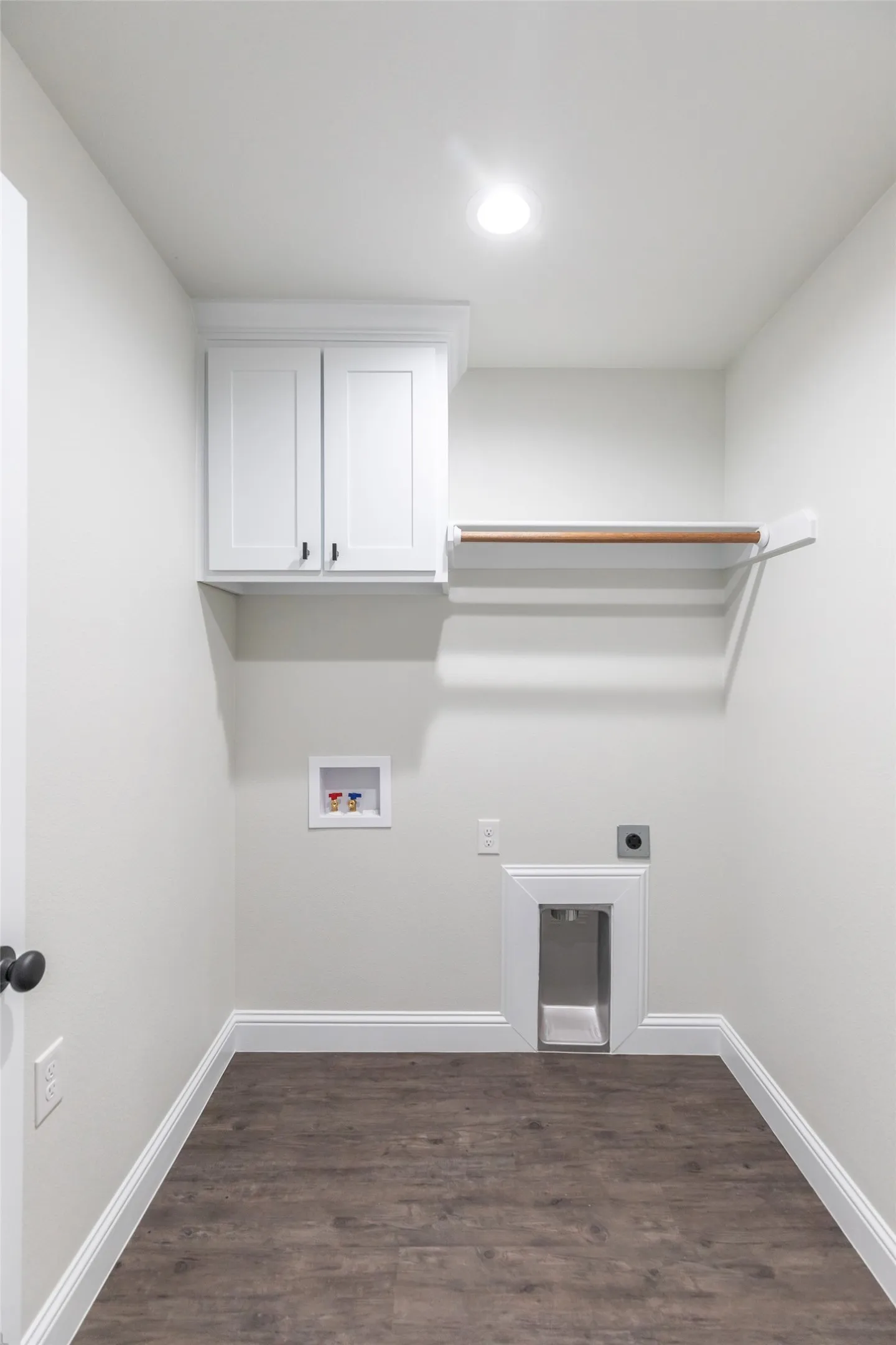 Laundry room featuring wood-finish flooring, white cabinetry with dark hardware, a built-in hanging rod, and recessed lighting