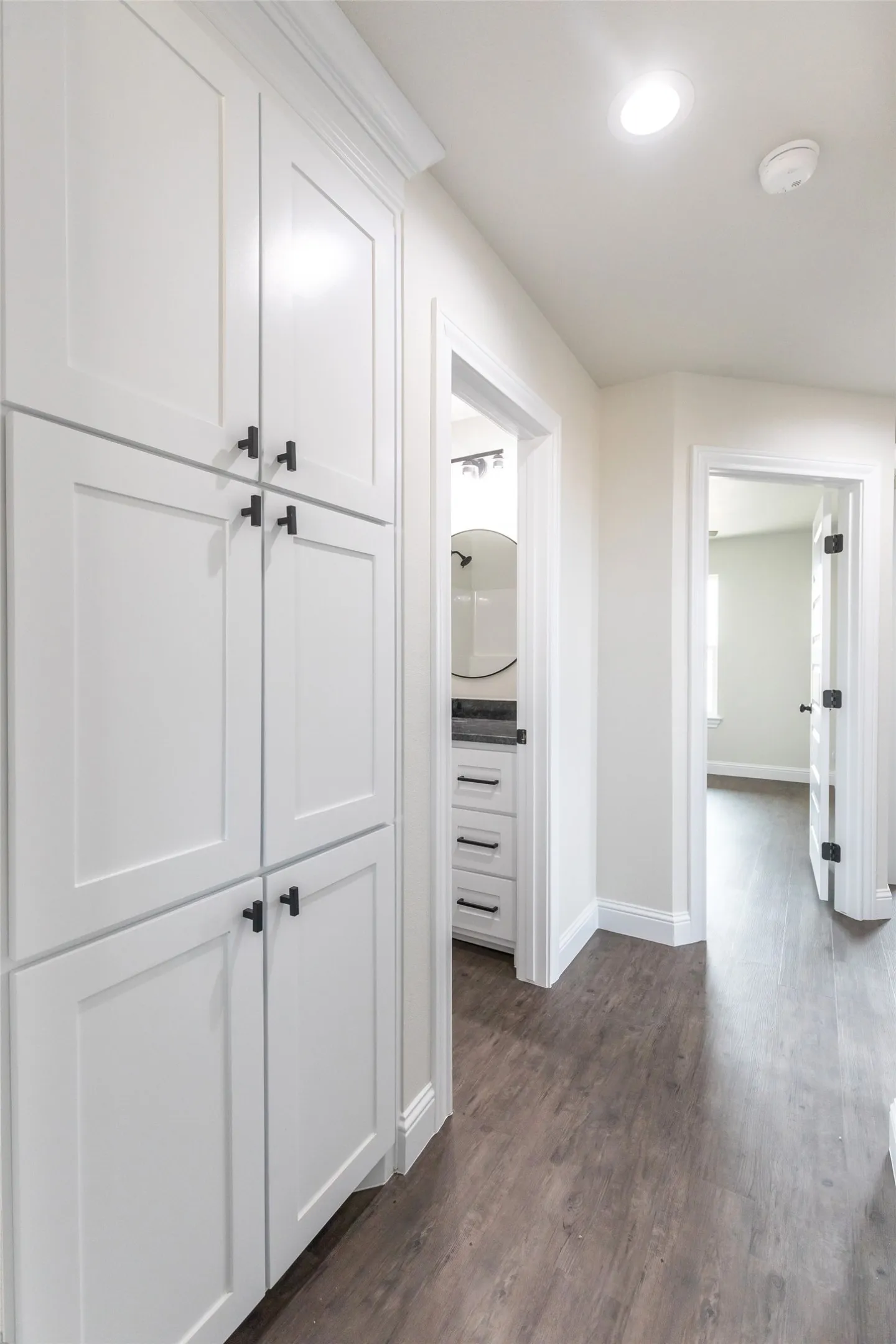 Hallway featuring tall white cabinetry with matte black hardware, wood-finish flooring, and recessed lighting